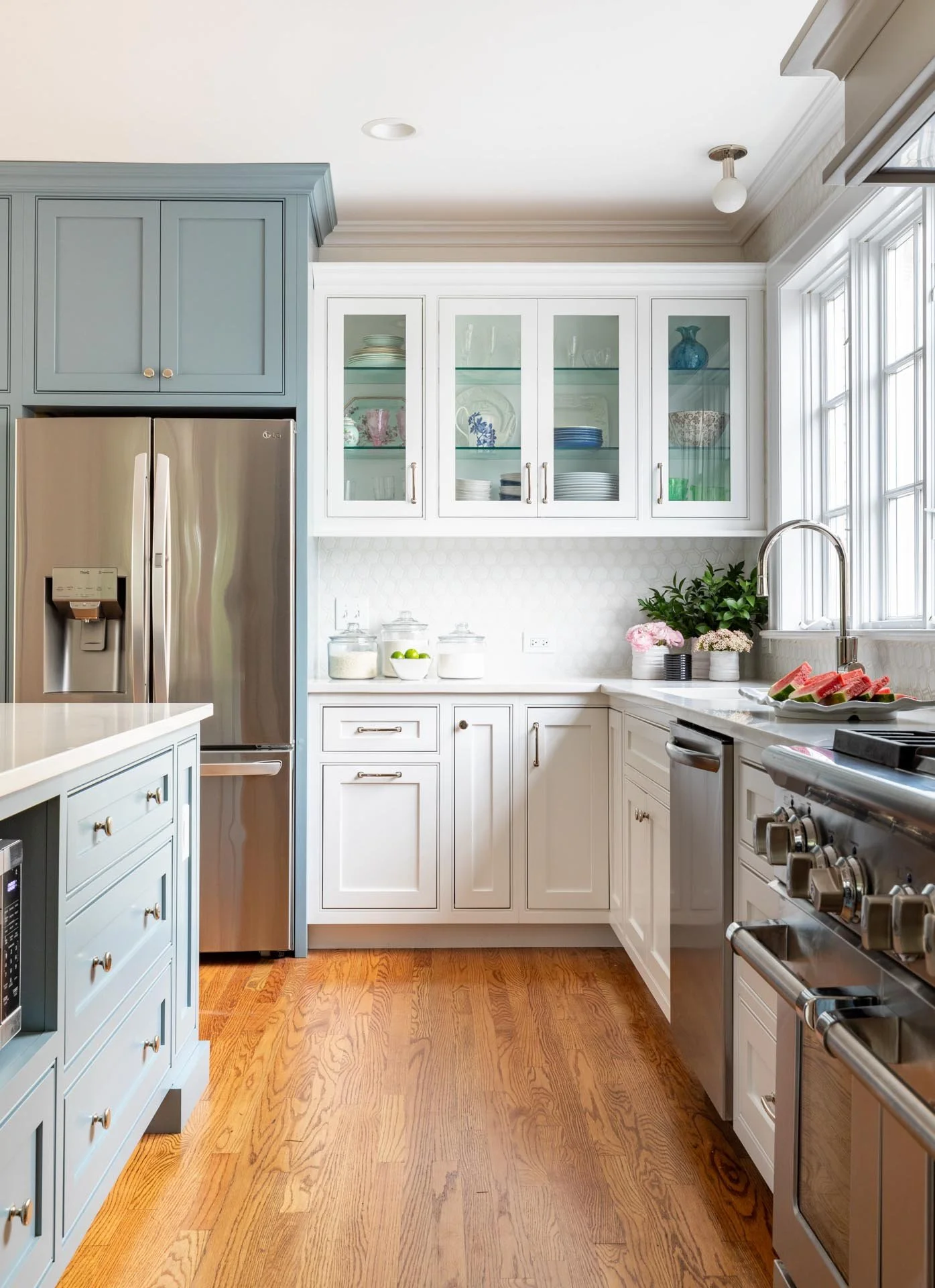 Lake Forest IL transitional kitchen featuring white cabinets with glass fronts, blue island cabinetry, stainless steel appliances, and quartz countertops, designed by Wendy Nobriga Interiors.