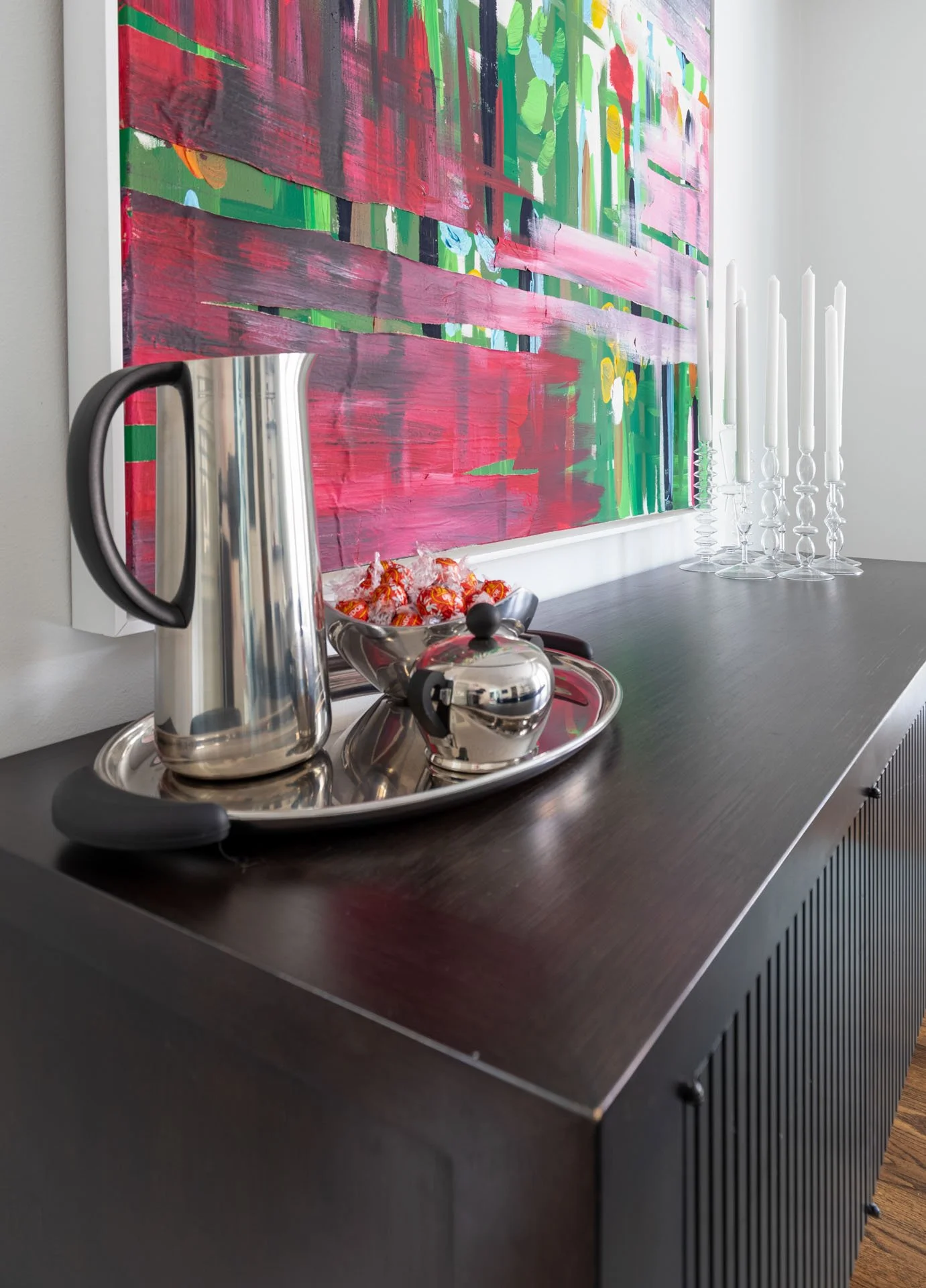 Dining room in Edgebrook, Chicago, IL showing a detail of the sideboard with silver tray, glass candlesticks, and bold modern artwork. Design by Wendy Nobriga Interiors.