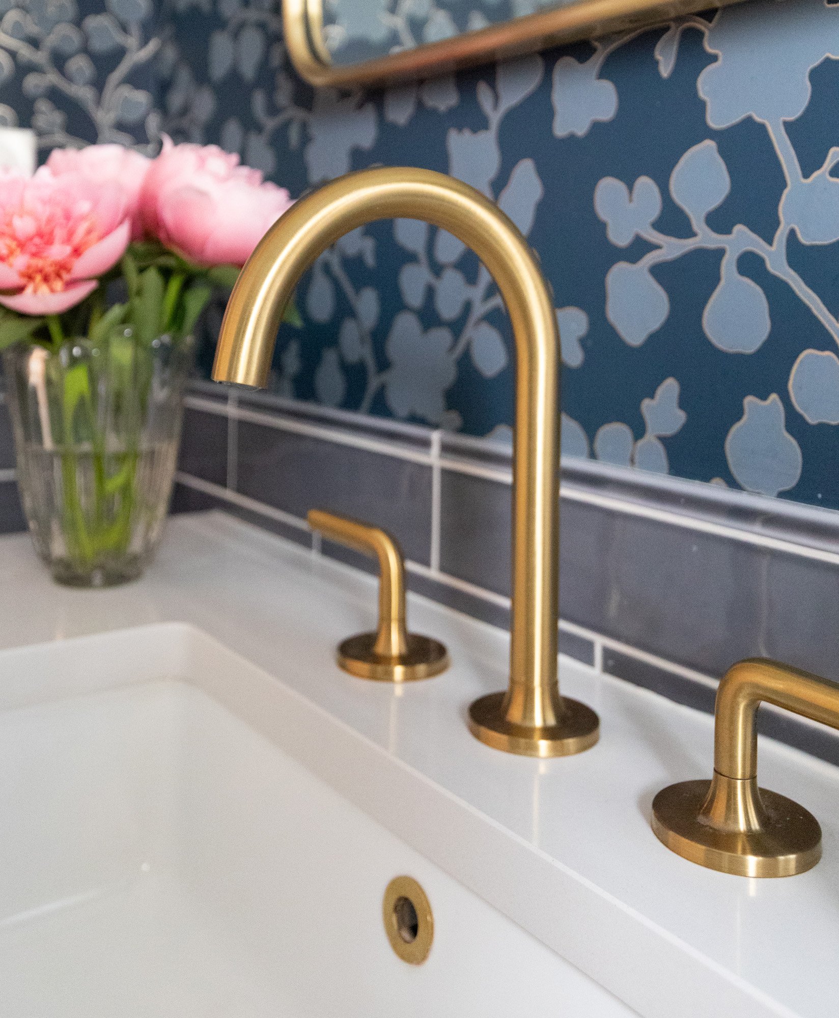 Quartz vanity countertop with a brass faucet, blue ceramic tile, and blue patterned wallpaper in a North Edgebrook Chicago bathroom, designed by Wendy Nobriga Interiors.