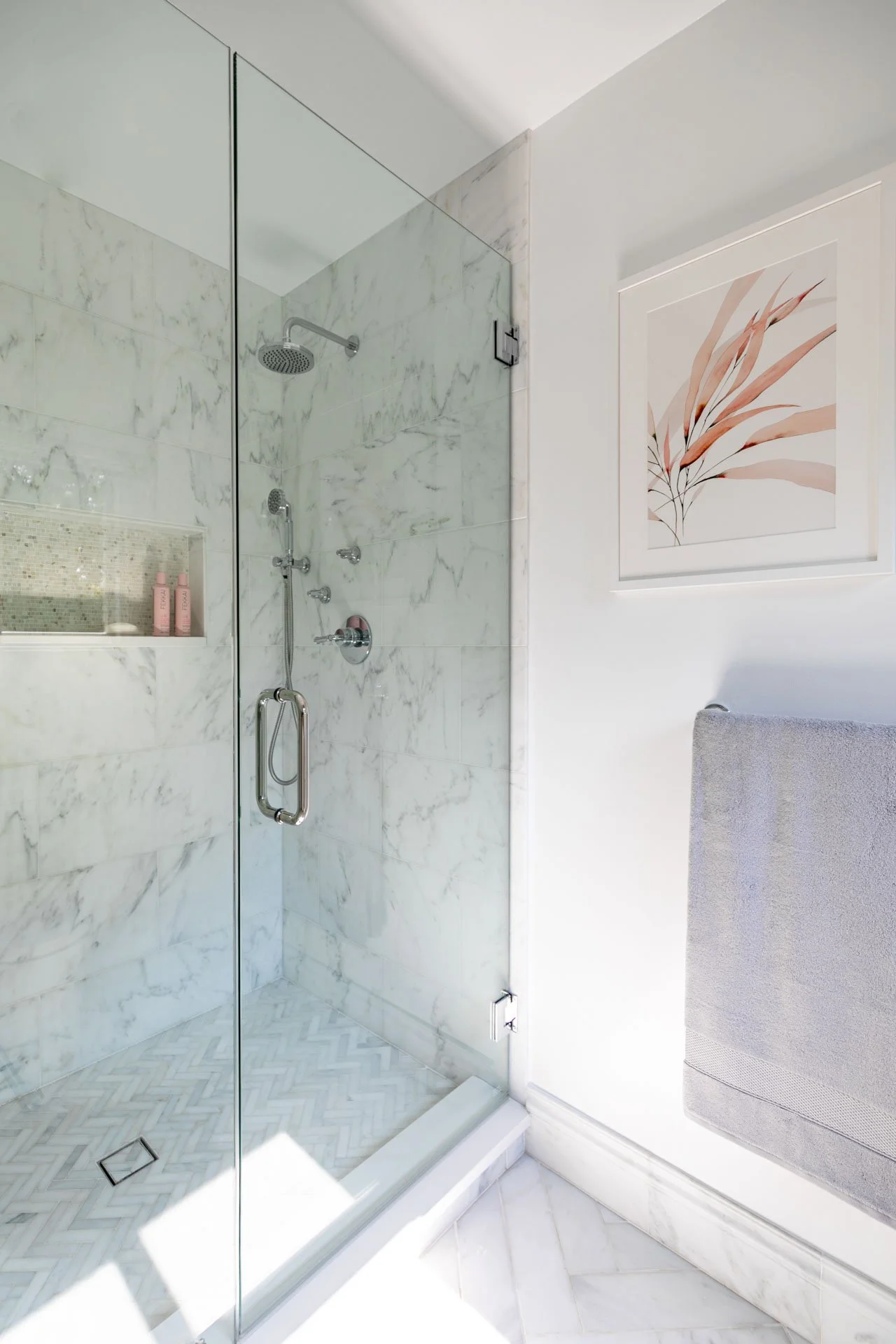 Northbrook IL primary bathroom marble shower with glass door, built-in niche, chrome fixtures, and modern wall art, designed by Wendy Nobriga Interiors