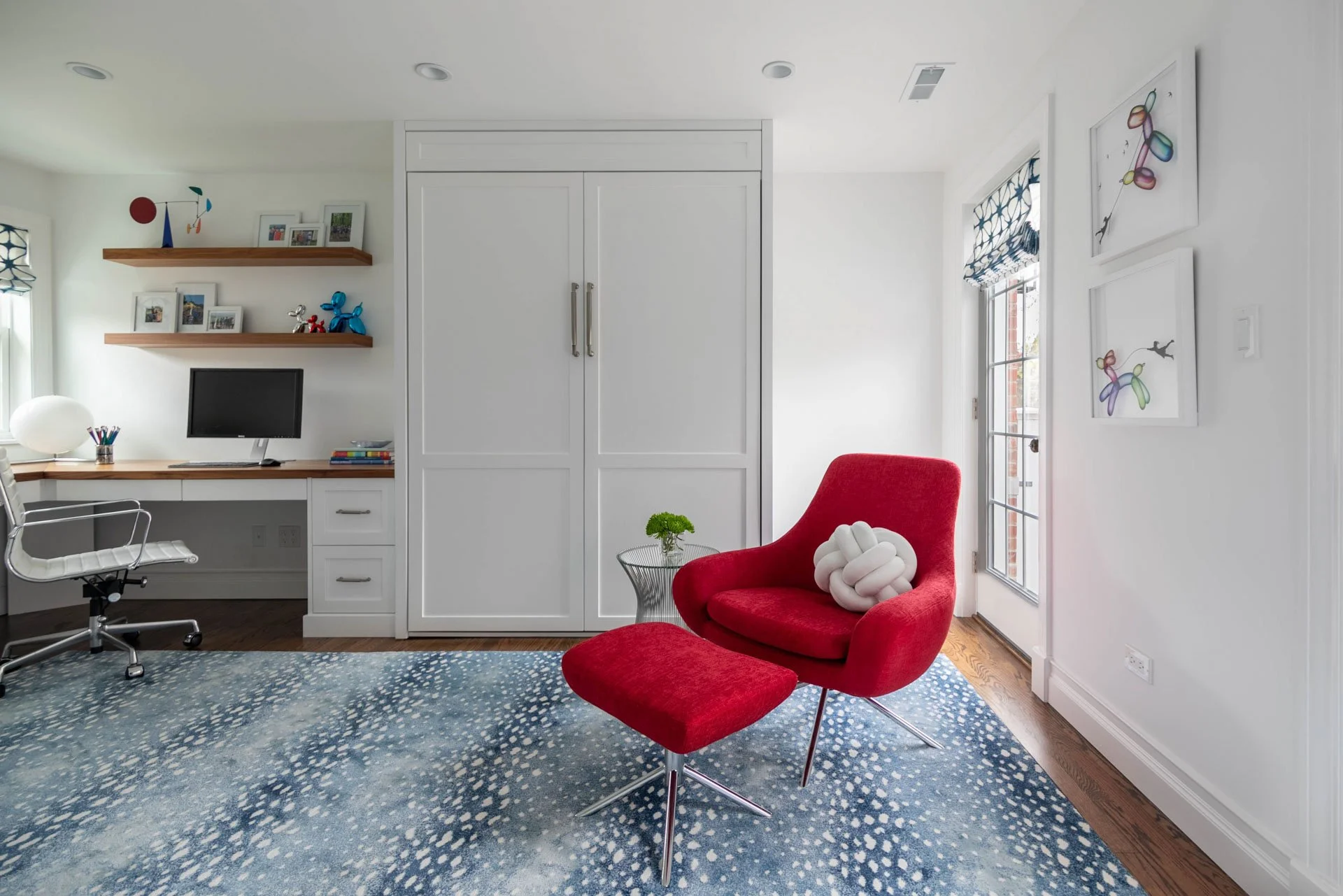 Guest bedroom and office in Edgebrook, Chicago, IL with built-in desk, floating shelves, red accent chair and ottoman, and blue patterned rug, designed by Wendy Nobriga Interiors.