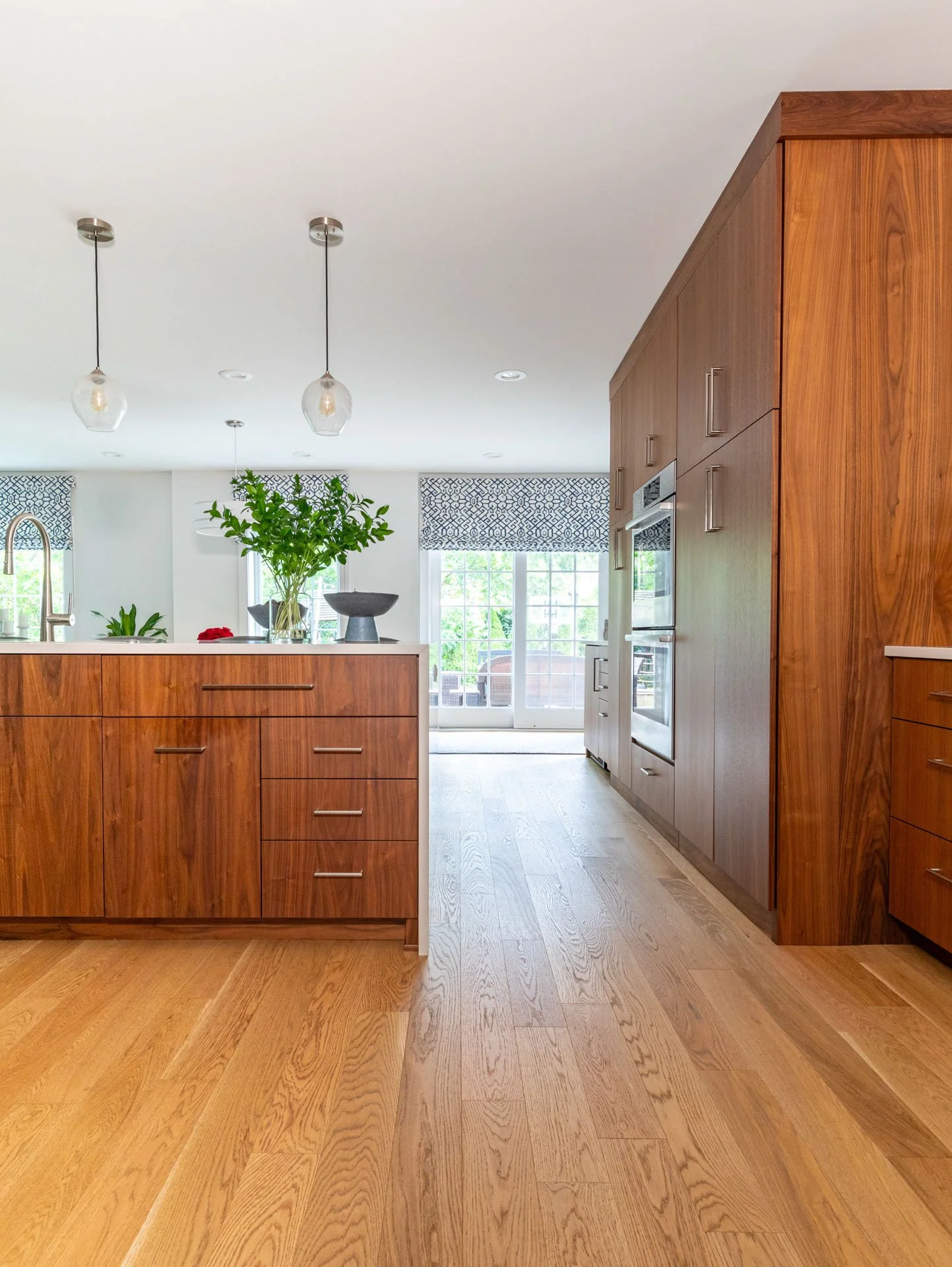 Wildwood Chicago IL kitchen view toward patio doors, featuring walnut island cabinetry, pendant lights, and wood flooring, designed by Wendy Nobriga Interiors.