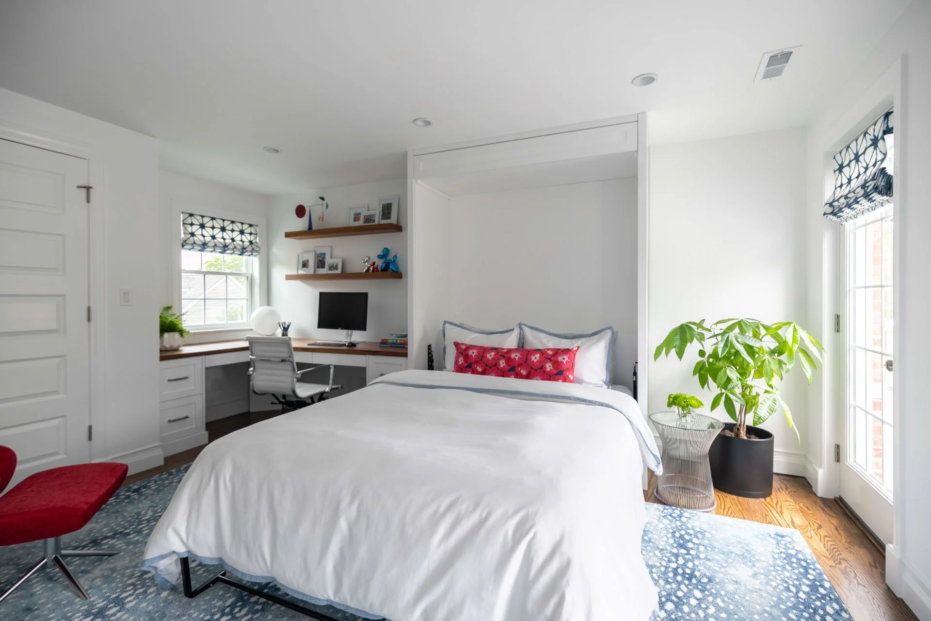Guest bedroom and office in Edgebrook, Chicago, IL with Murphy bed pulled down, crisp white bedding, bold red accent pillow, built-in desk, and greenery, designed by Wendy Nobriga Interiors.