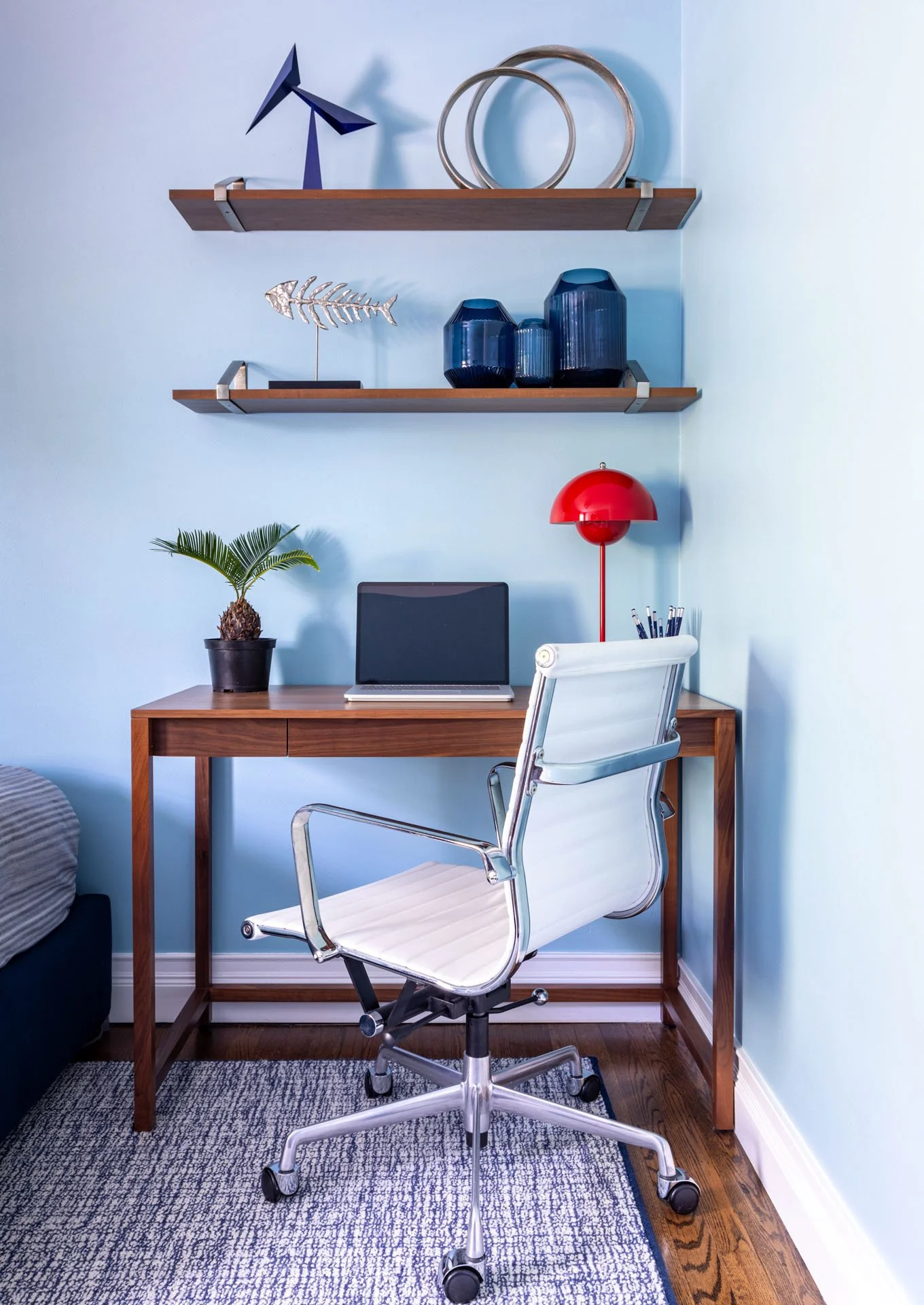 Kid’s bedroom in Edgebrook, Chicago, IL with walnut desk, white swivel chair, red lamp, floating shelves, and blue wall accents, designed by Wendy Nobriga Interiors.