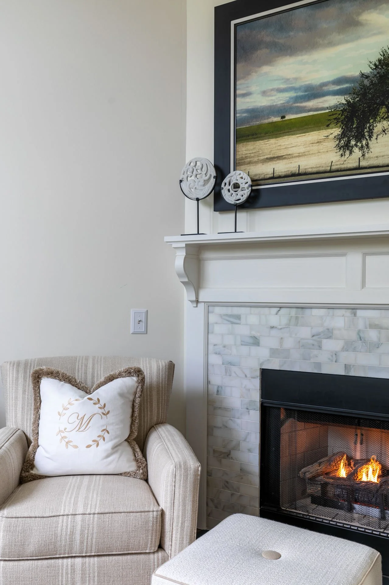 Des Plaines IL living room with striped armchair, monogrammed pillow, marble fireplace surround, and artwork above mantel designed by Wendy Nobriga Interiors