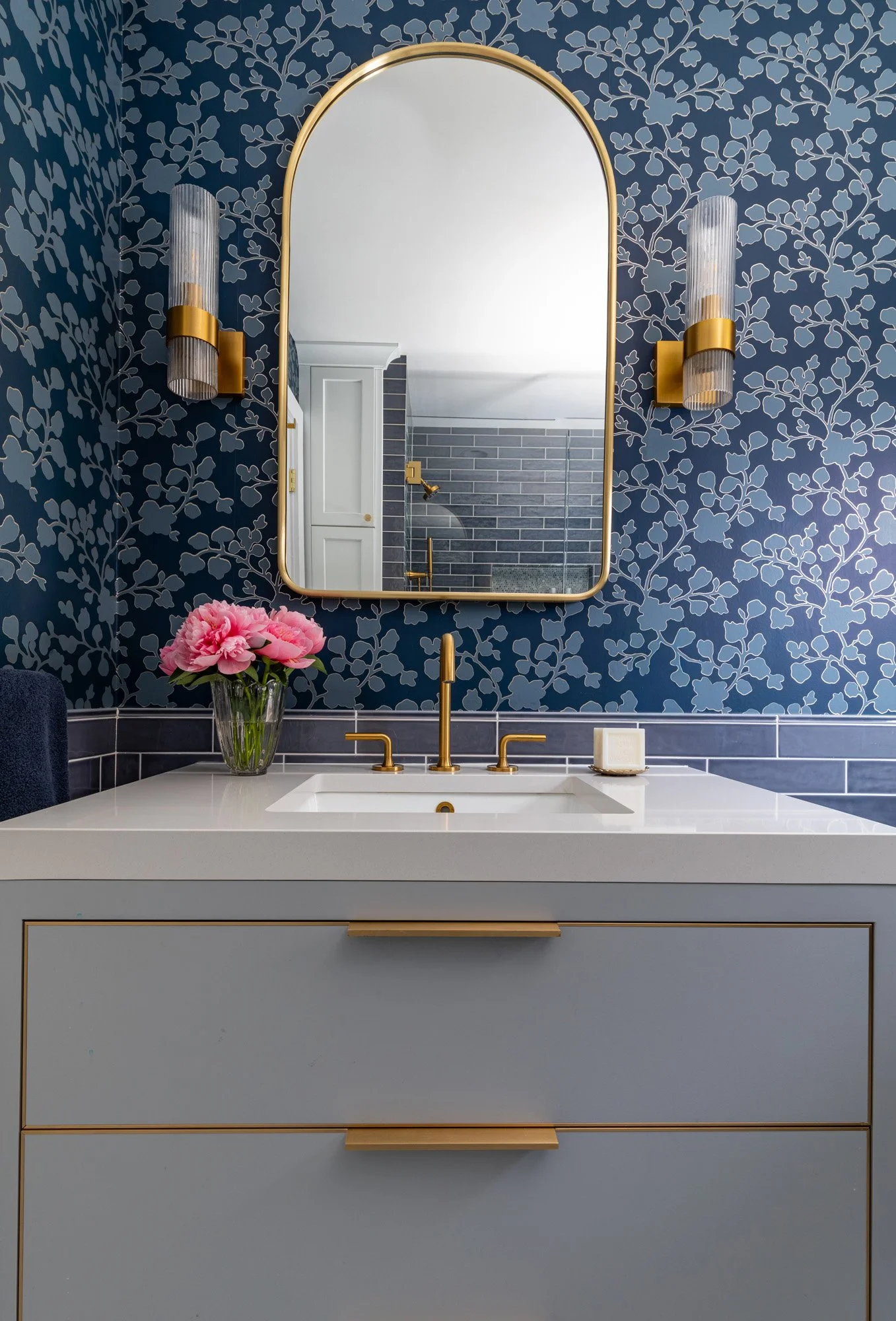 Custom bathroom vanity with a modern mirror, brass sconces, and blue patterned wallpaper in a North Edgebrook Chicago home, designed by Wendy Nobriga Interiors.