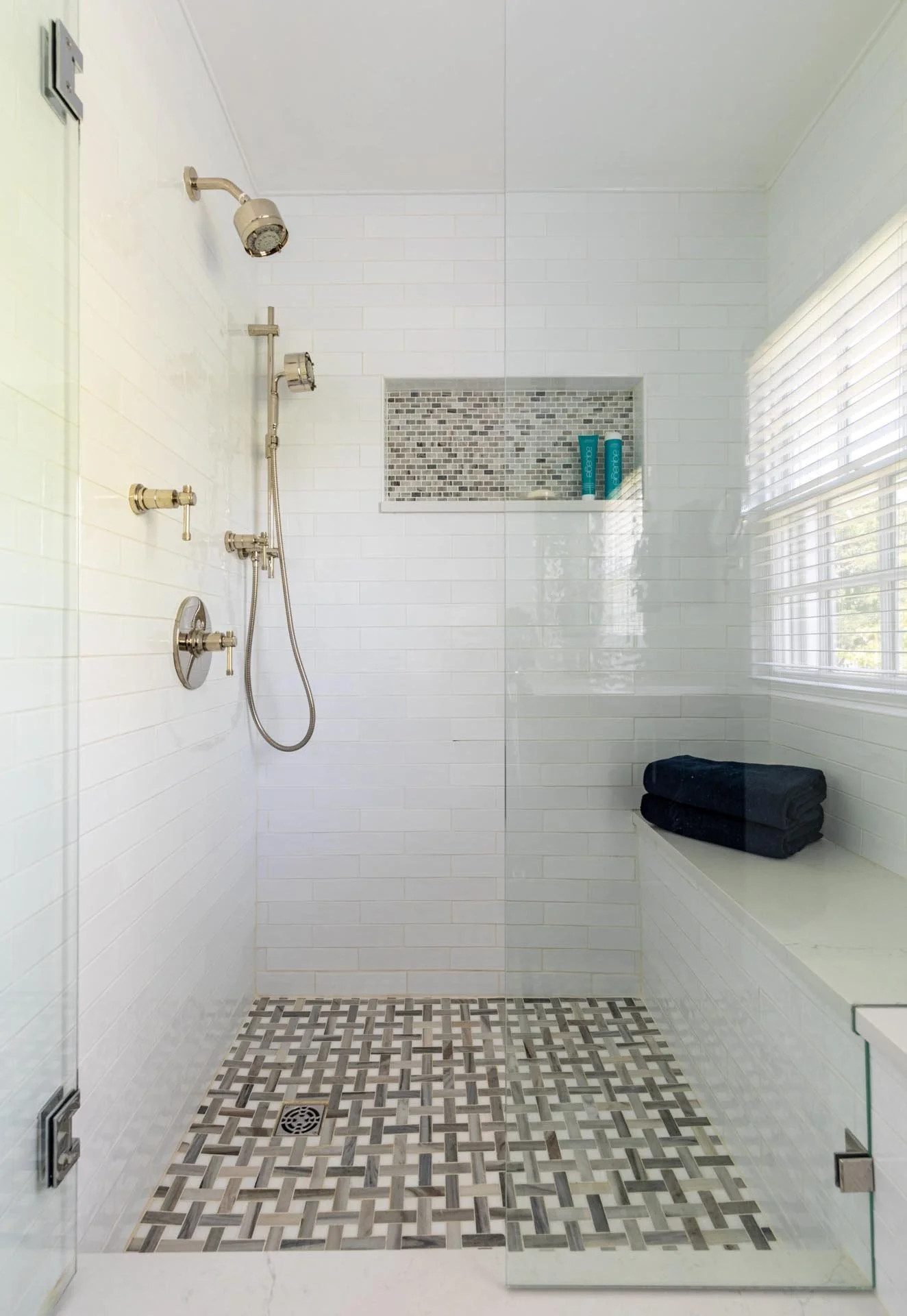 Lake Forest IL primary bathroom walk-in shower with white subway tile, mosaic accent niche, and marble patterned floor tile, designed by Wendy Nobriga Interiors.