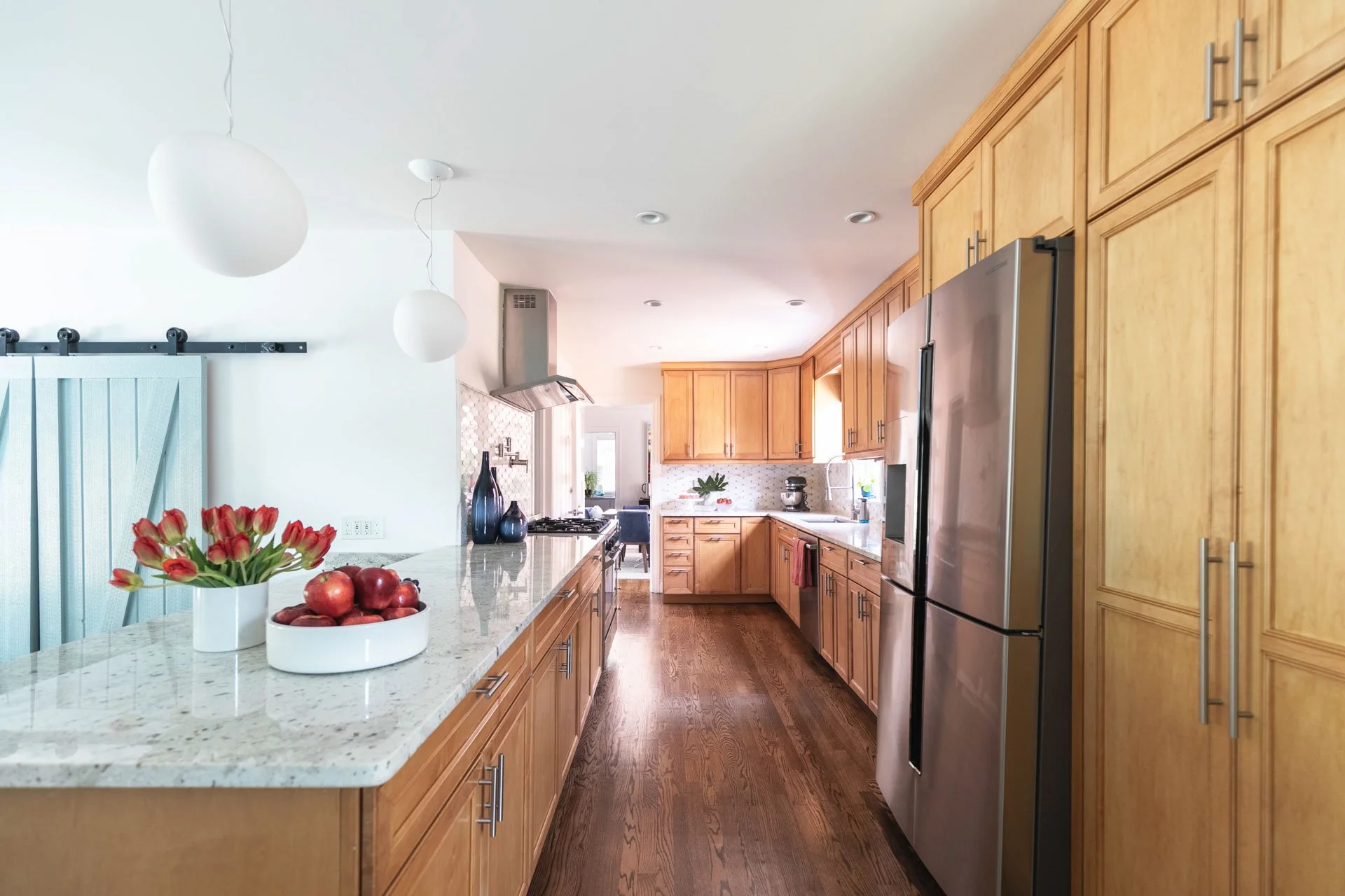 Kitchen in Edgebrook, Chicago, IL with maple cabinets, white granite countertops, stainless steel appliances, and a peninsula accented with red tulips and apples. Design by Wendy Nobriga Interiors.