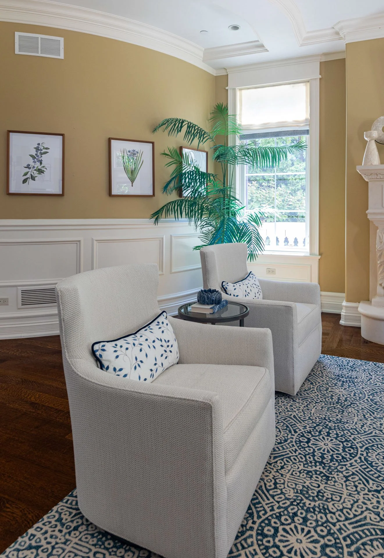 Lincolnwood IL family room with two white accent chairs blue patterned rug and framed botanical art designed by Wendy Nobriga Interiors