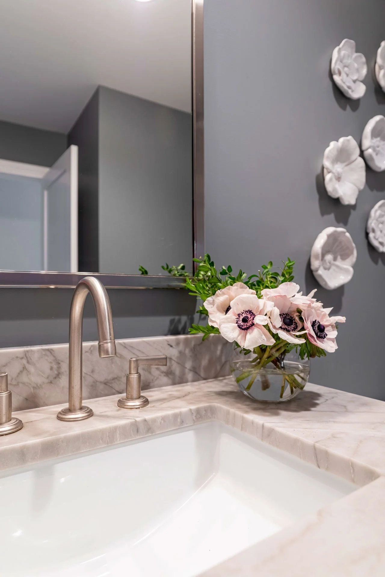 Close-up of quartzite powder room sink with brushed nickel faucet and fresh flowers designed by Wendy Nobriga Interiors in La Grange IL.
