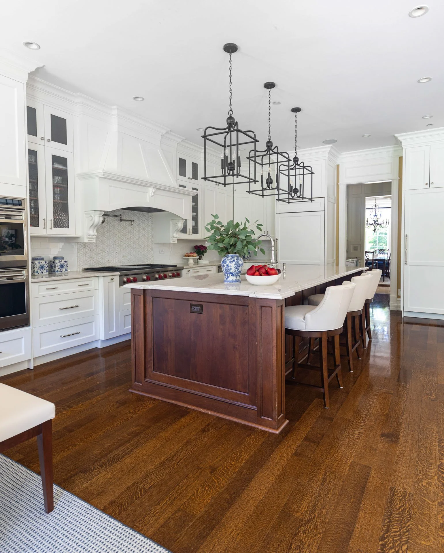Lincolnwood IL kitchen with a dark wood island topped with quartzite countertops, white cabinetry, double ovens, and black lantern pendants, designed by Wendy Nobriga Interiors.