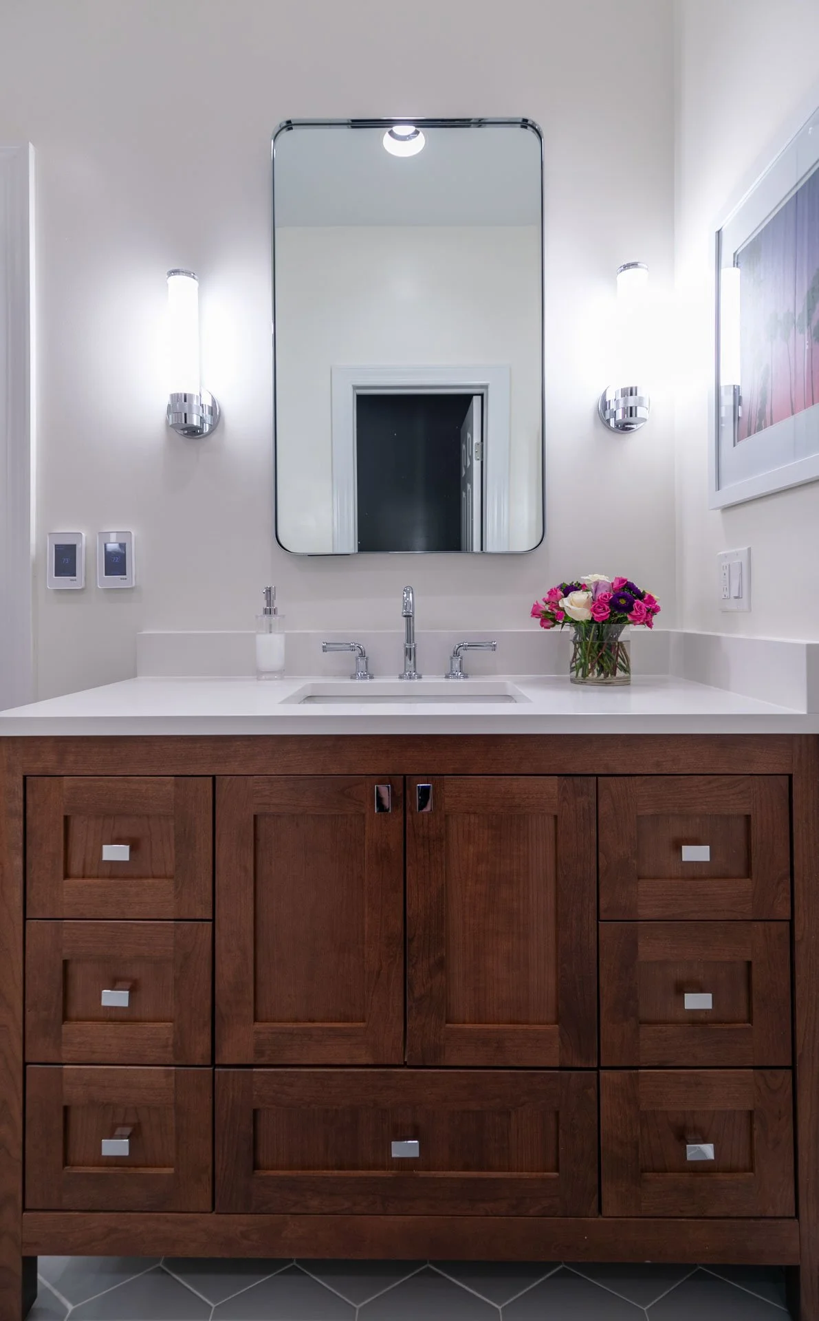 Lake View Chicago primary bathroom vanity with rich wood cabinetry, white quartz countertop, chrome faucet, modern sconces, and fresh pink and white flowers, designed by Wendy Nobriga Interiors