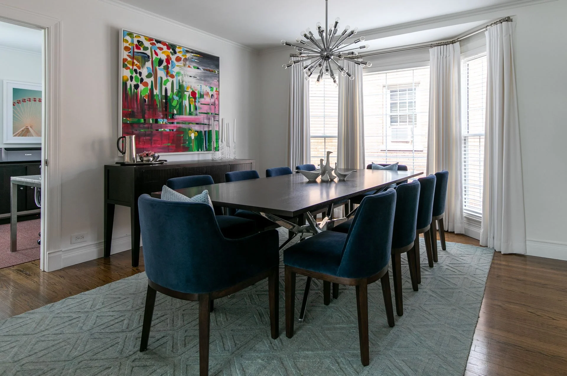 Dining room in Edgebrook, Chicago, IL with a modern dark wood table, navy chairs, bold abstract artwork, and a starburst chandelier. Design by Wendy Nobriga Interiors.
