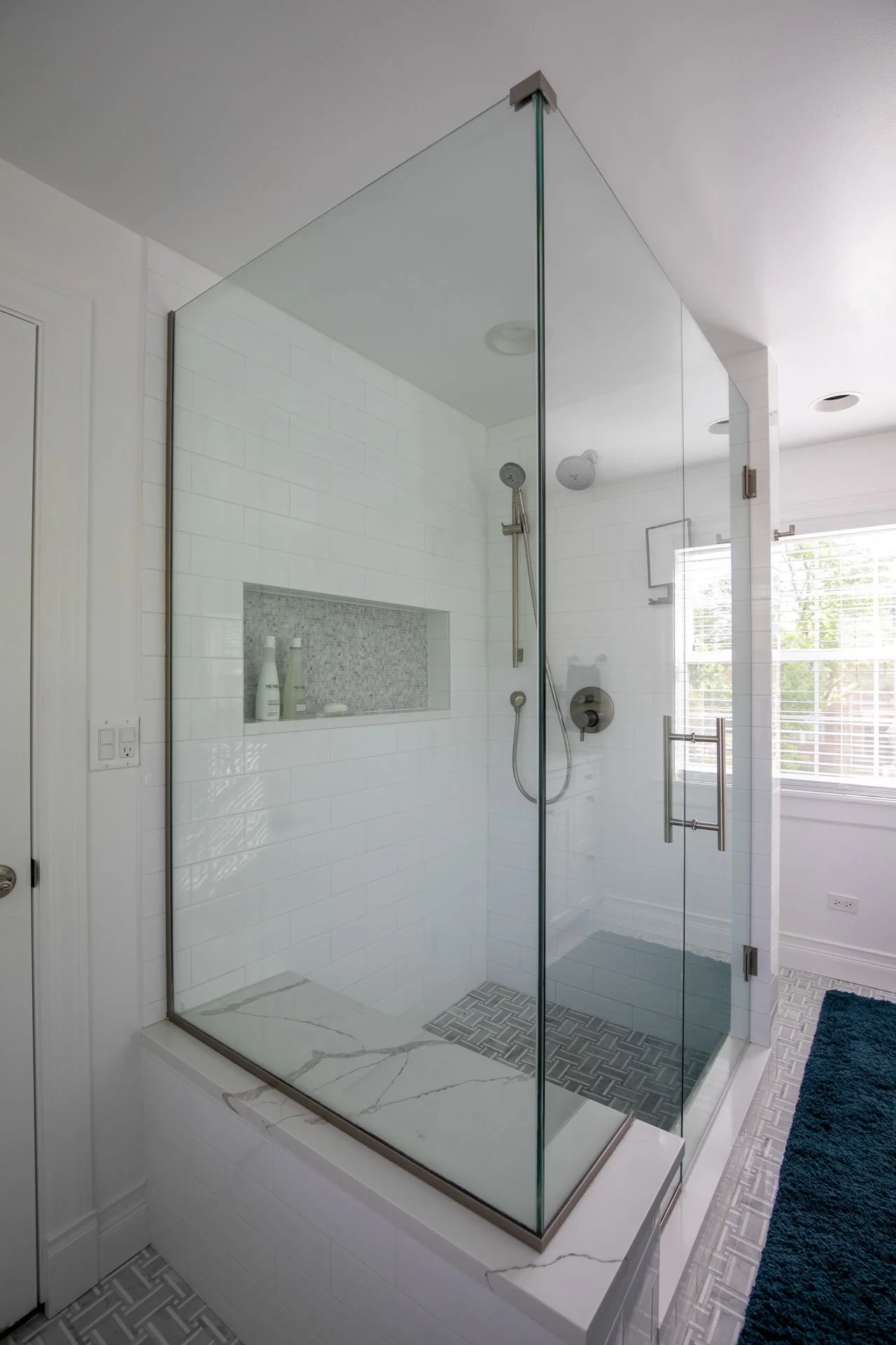Glass-enclosed primary bathroom shower with quartz bench, white subway tile walls, and marble mosaic floor tile, Edgebrook, Chicago, IL, designed by Wendy Nobriga Interiors.