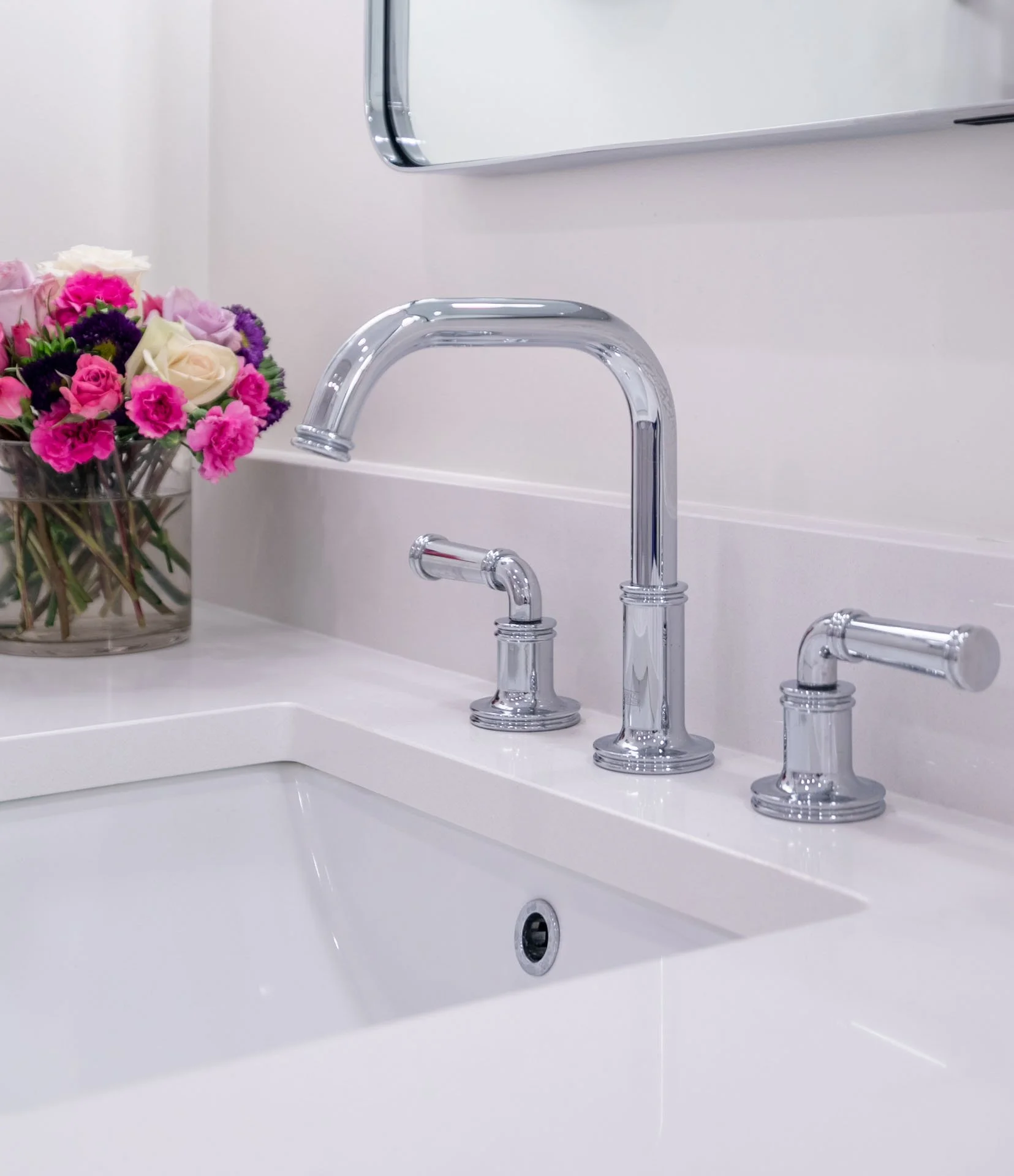 Lake View Chicago primary bathroom detail with chrome widespread faucet, white quartz countertop, and fresh floral accent in glass vase, designed by Wendy Nobriga Interiors