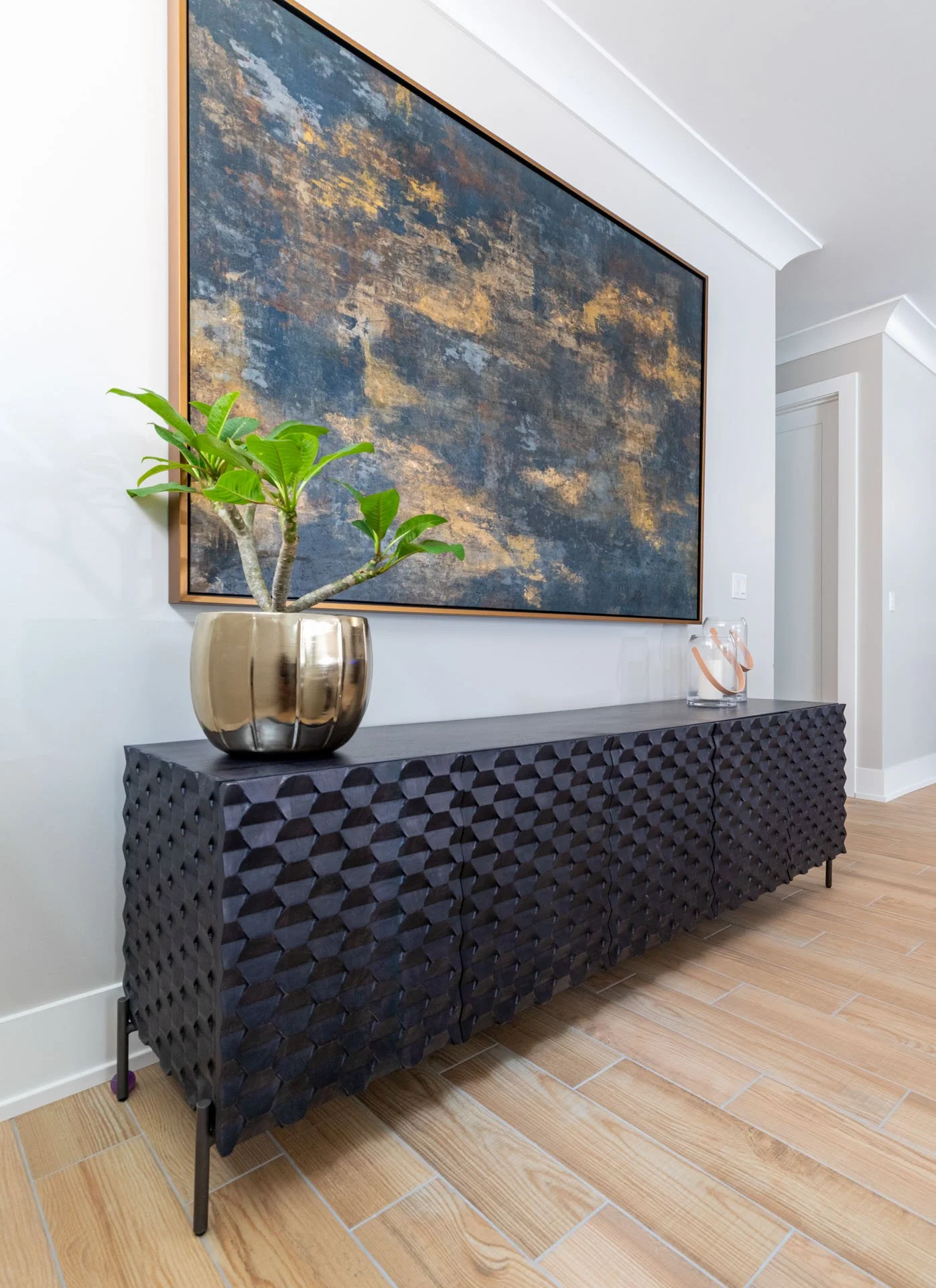 Detail of Roscoe Village Chicago basement family room featuring a textured black console, metallic planter with greenery, and large abstract artwork, designed by Wendy Nobriga Interiors.