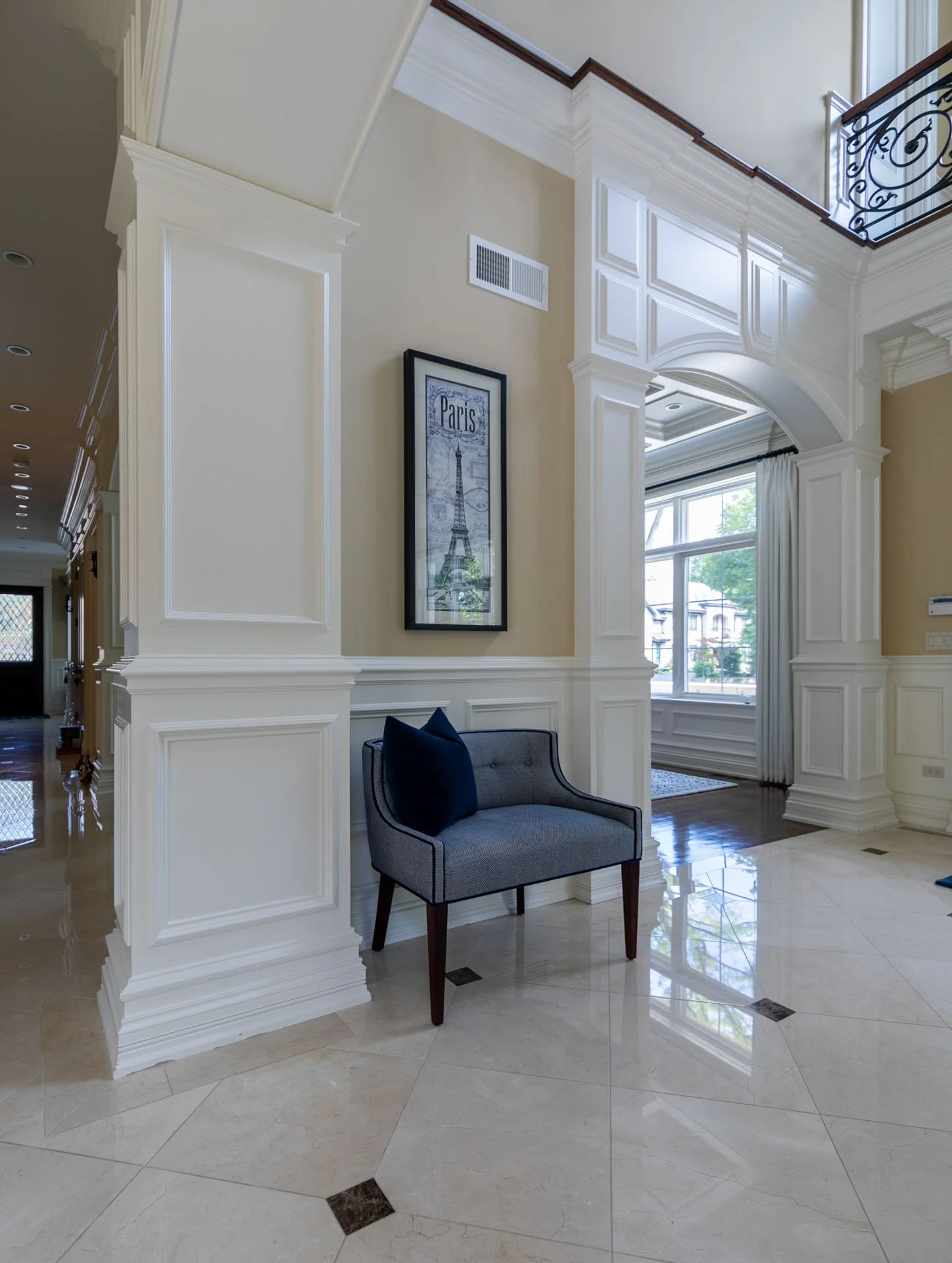 Lincolnwood IL foyer with marble tile floors, white millwork, blue accent chair, and Paris artwork, designed by Wendy Nobriga Interiors.