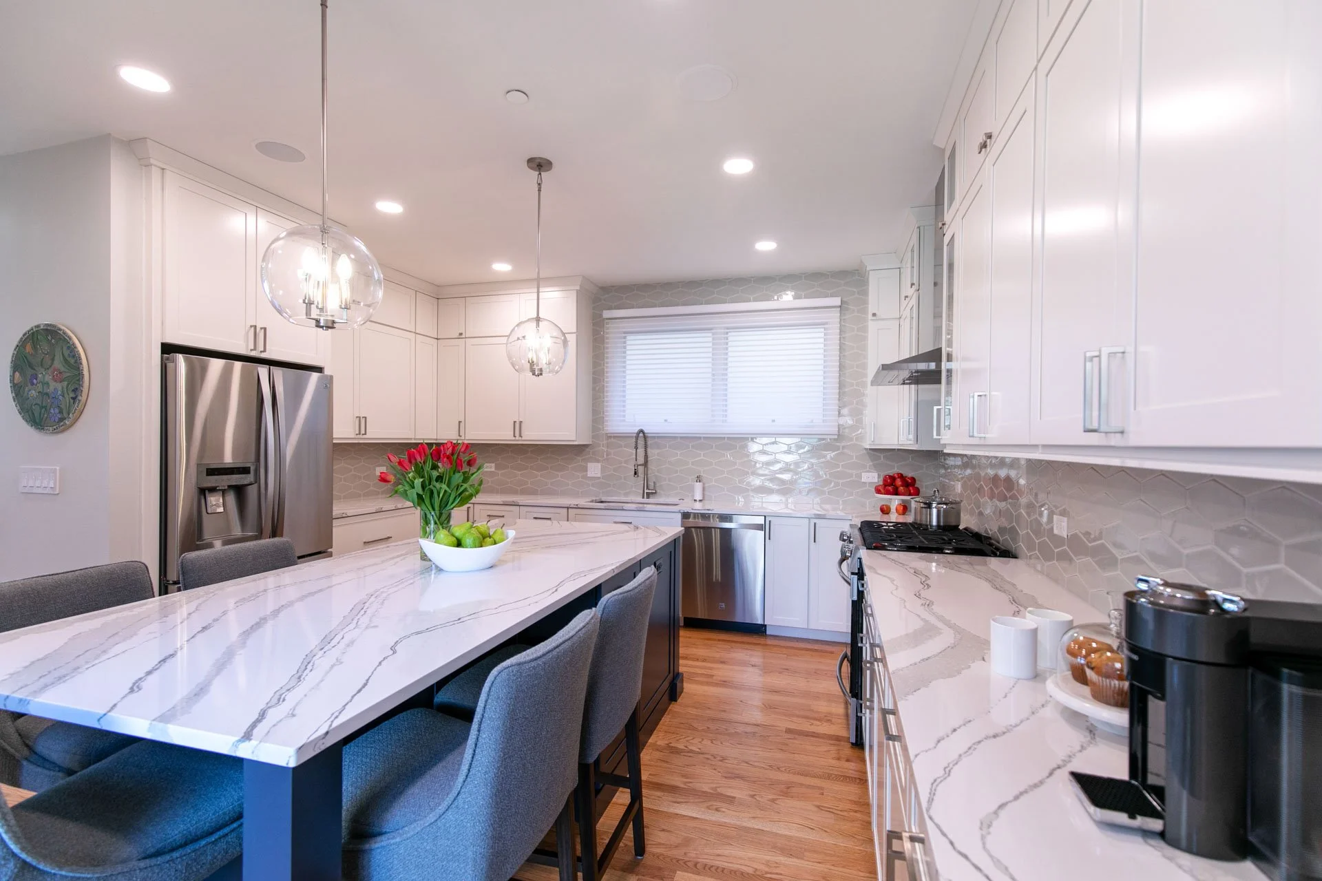 Oak Park, IL townhouse kitchen with large quartz island, modern pendant lighting, white cabinets, and stainless steel appliances, designed by Wendy Nobriga Interiors