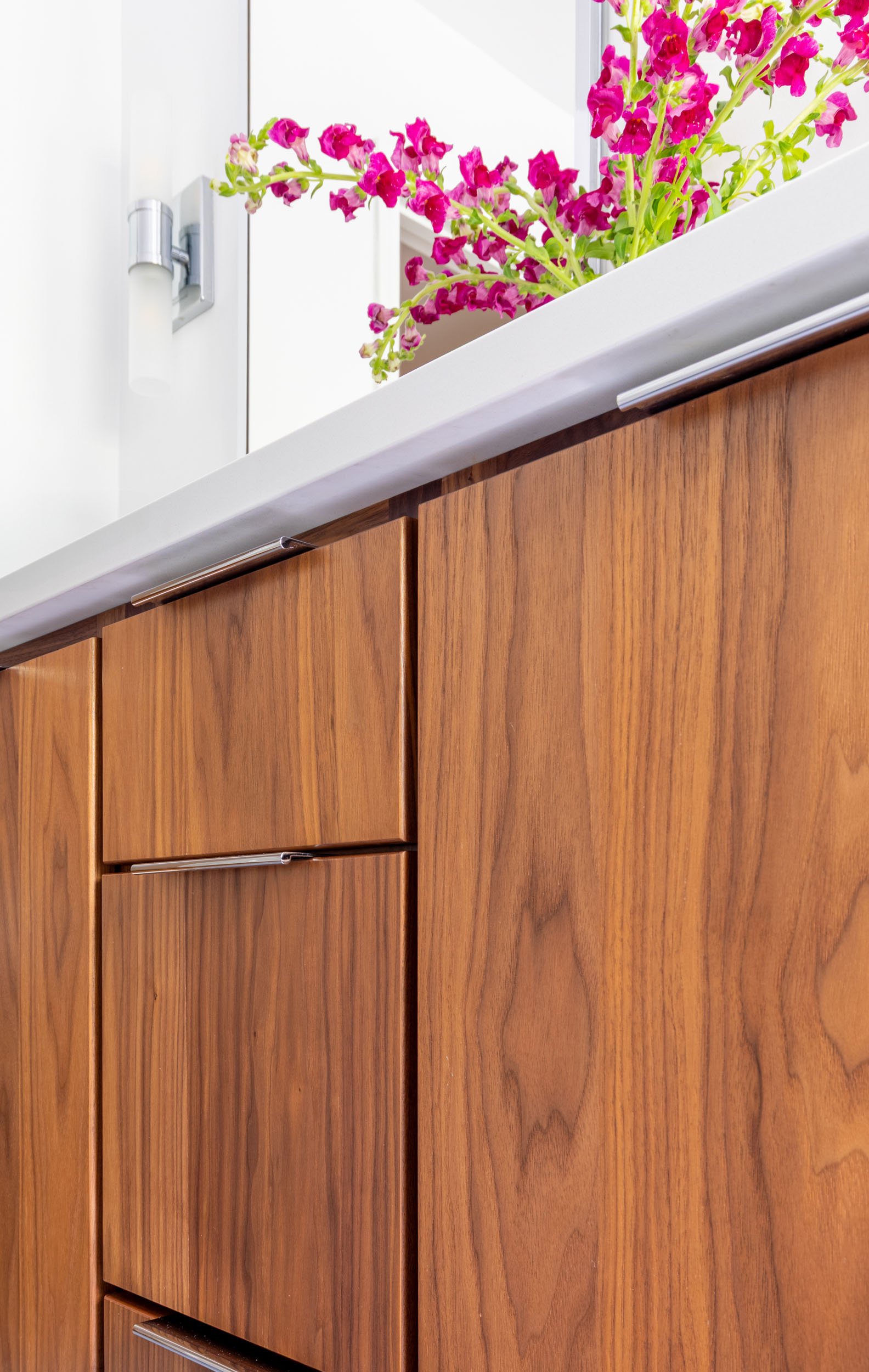 Walnut bathroom vanity detail in a kids hall bathroom in Northbrook, Illinois with modern flat-panel cabinetry and integrated pulls. Design by Wendy Nobriga Interiors.