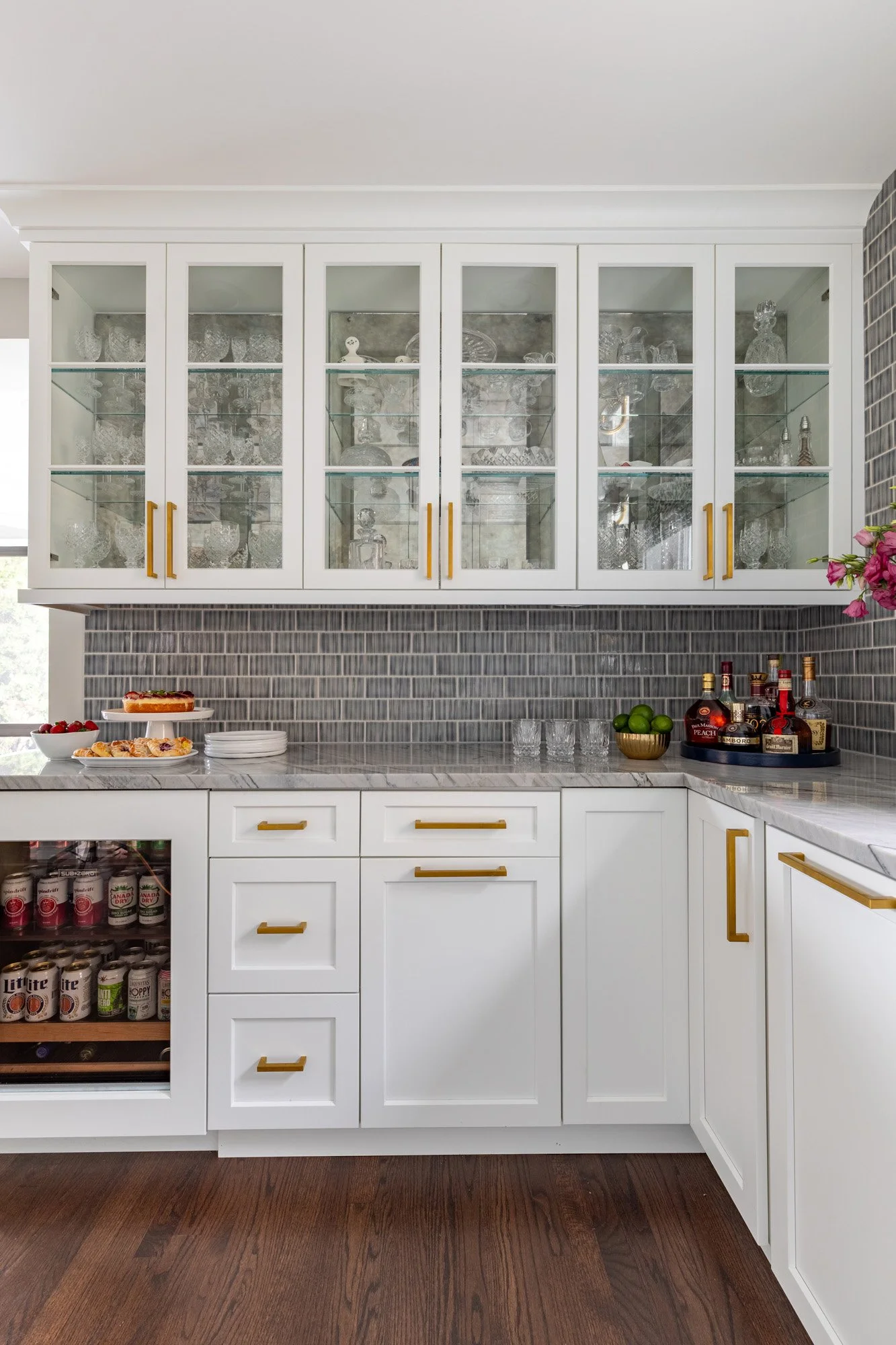 Custom glass display cabinetry in a North Edgebrook Chicago beverage center featuring quartzite countertops, blue handcrafted tile backsplash, and brass hardware, designed by Wendy Nobriga Interiors.