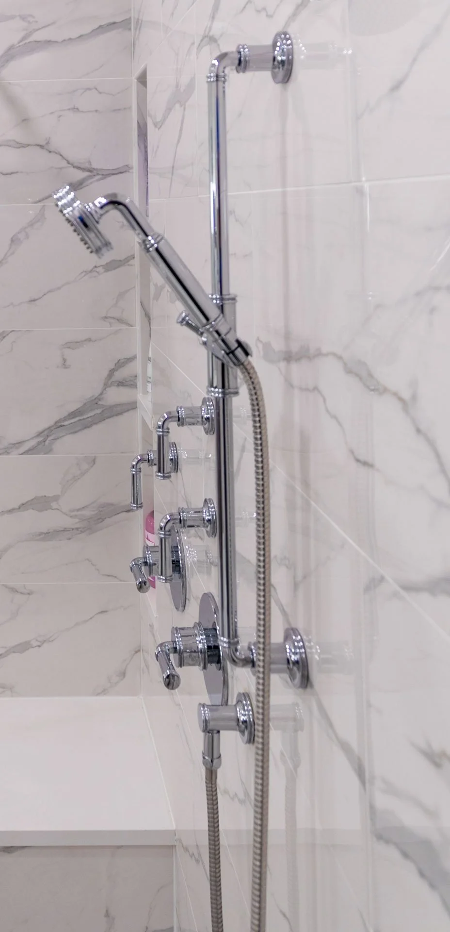 Lake View Chicago primary bathroom wet room shower system with handheld sprayer, multiple polished chrome controls, porcelain marble-look tile, and built-in bench, designed by Wendy Nobriga Interiors
