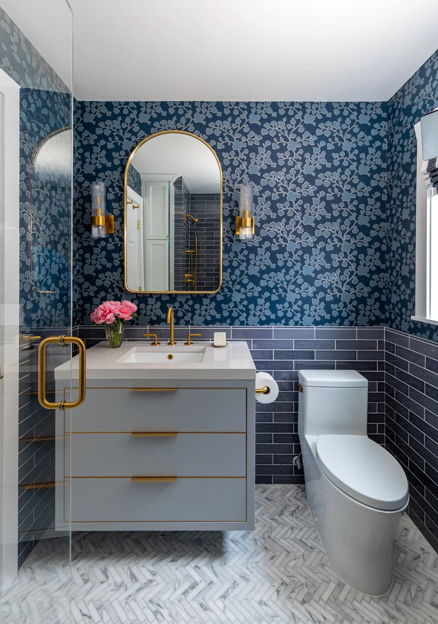 Modern first-floor bathroom in a North Edgebrook Chicago home featuring blue patterned wallpaper, a floating vanity, brass fixtures, custom lighting, and marble-mosaic flooring, designed by Wendy Nobriga Interiors.