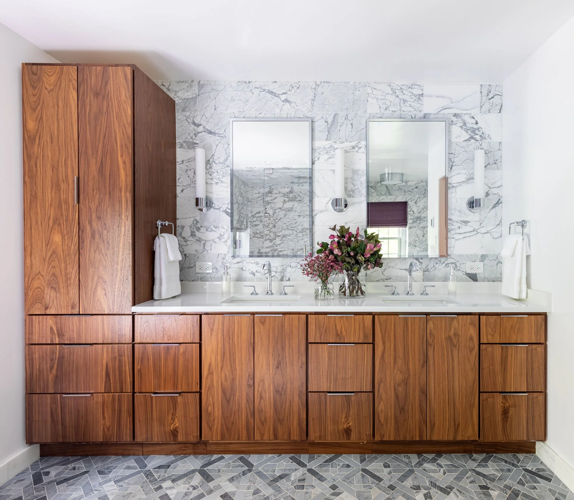 Primary bathroom in Northbrook, Illinois with custom walnut double vanity and marble slab backsplash. Design by Wendy Nobriga Interiors.