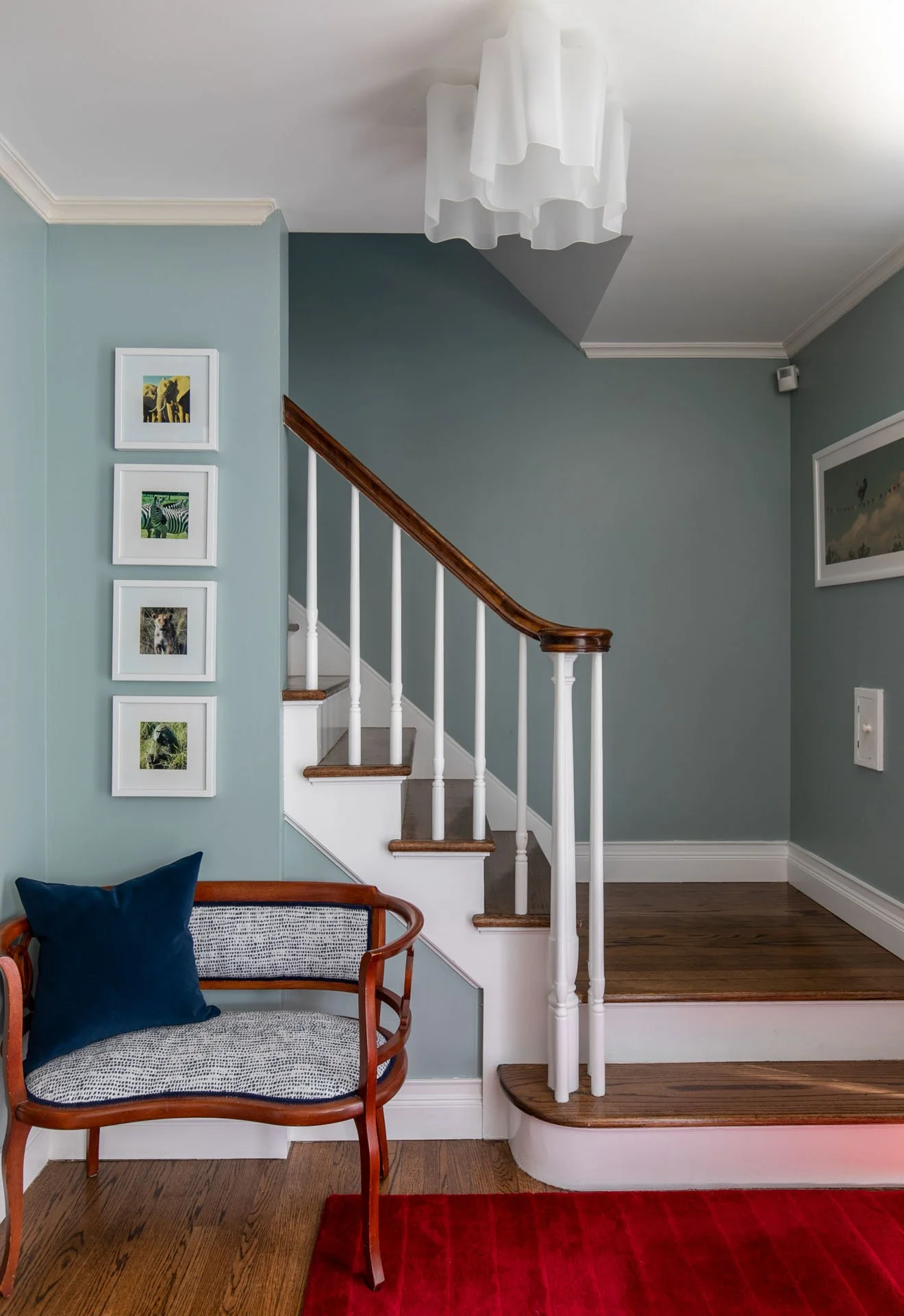 Edgebrook, Chicago, IL foyer design with light blue walls, wood staircase, red rug, and accent bench by Wendy Nobriga Interiors