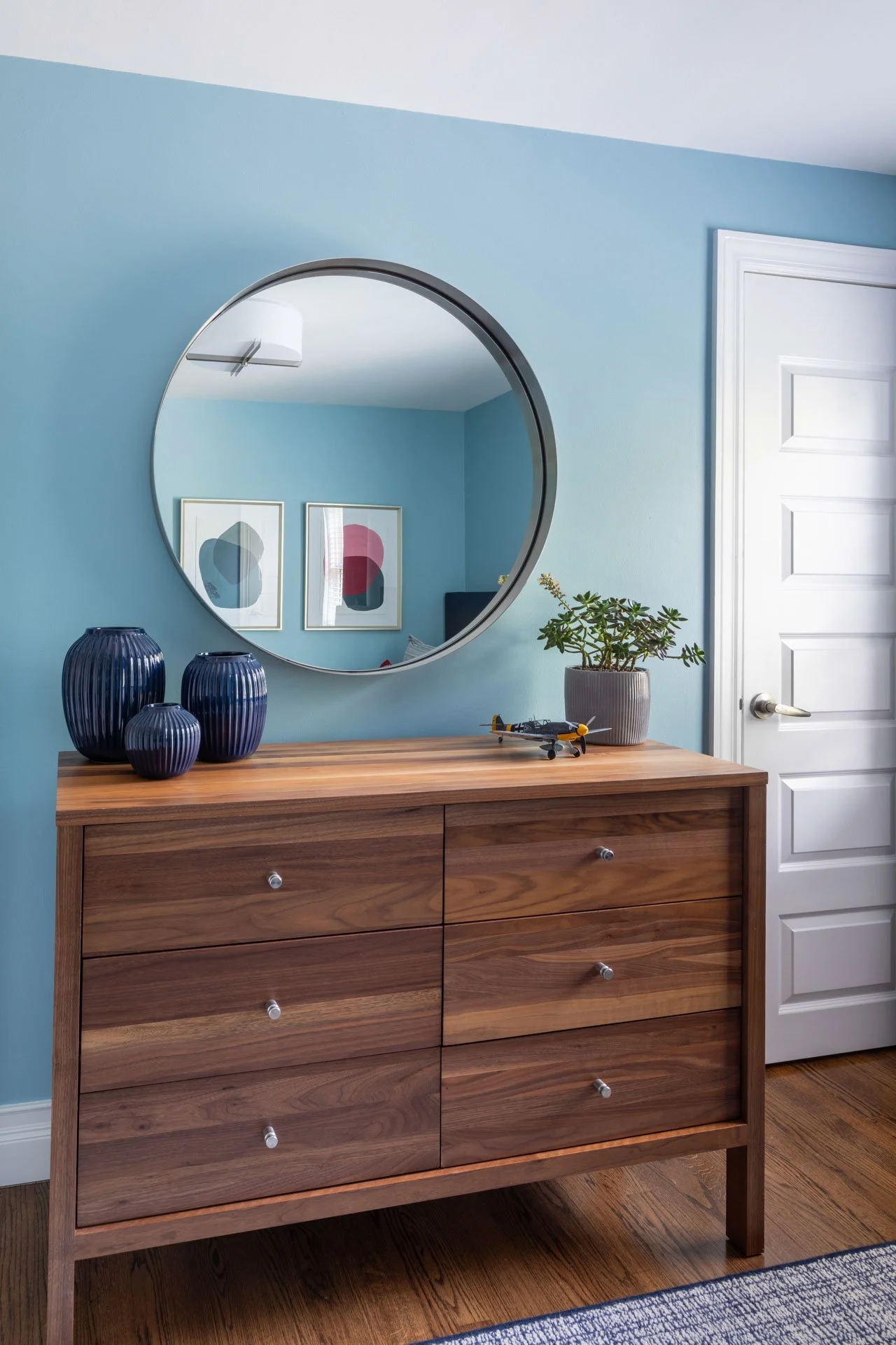 Kid’s bedroom in Edgebrook, Chicago, IL with walnut dresser, round mirror, blue vases, and modern accessories, designed by Wendy Nobriga Interiors.