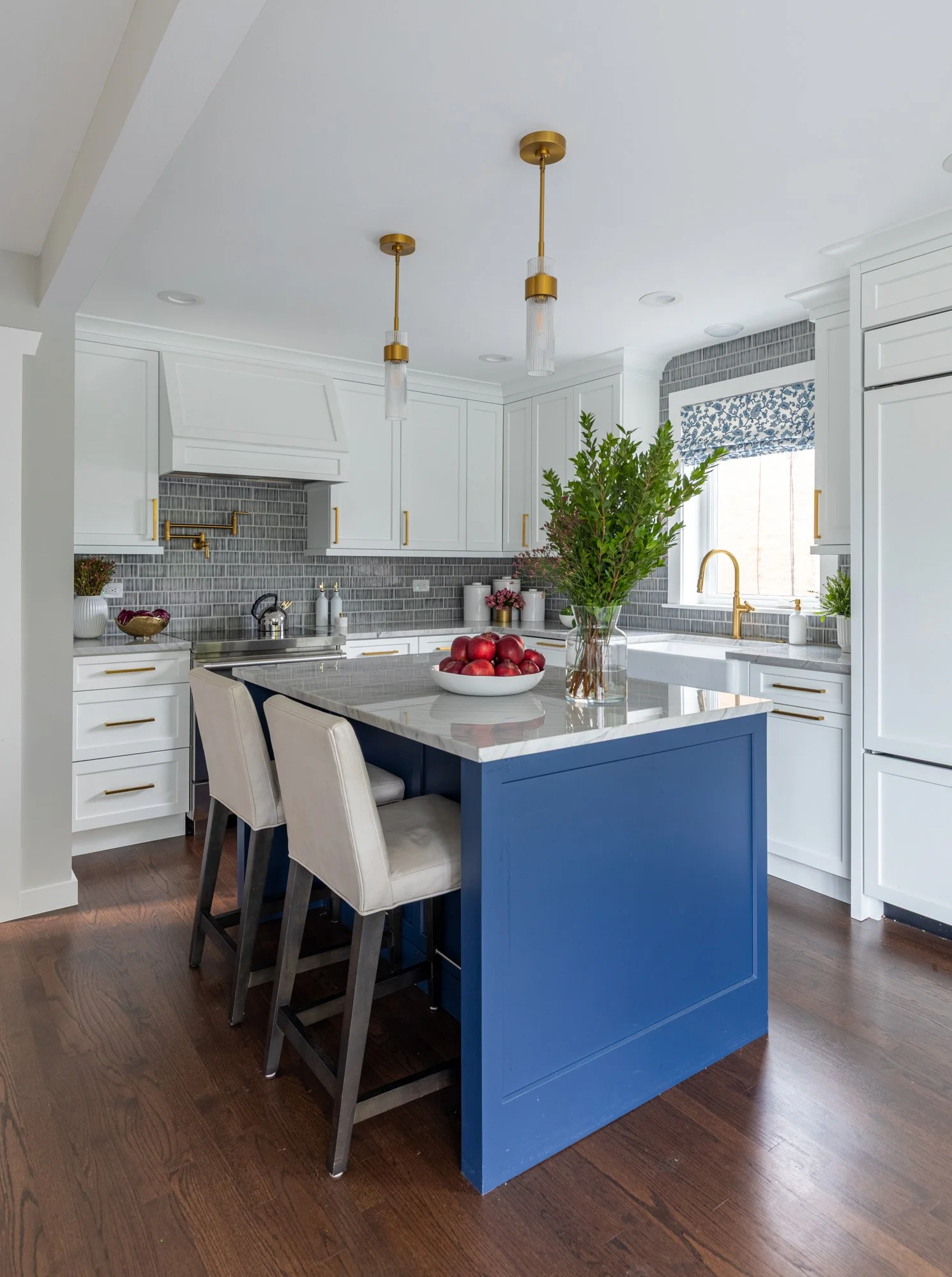 Custom North Edgebrook Chicago kitchen featuring white shaker cabinetry, a navy blue island, quartzite countertops, brass lighting, and an open-concept layout, designed by Wendy Nobriga Interiors.