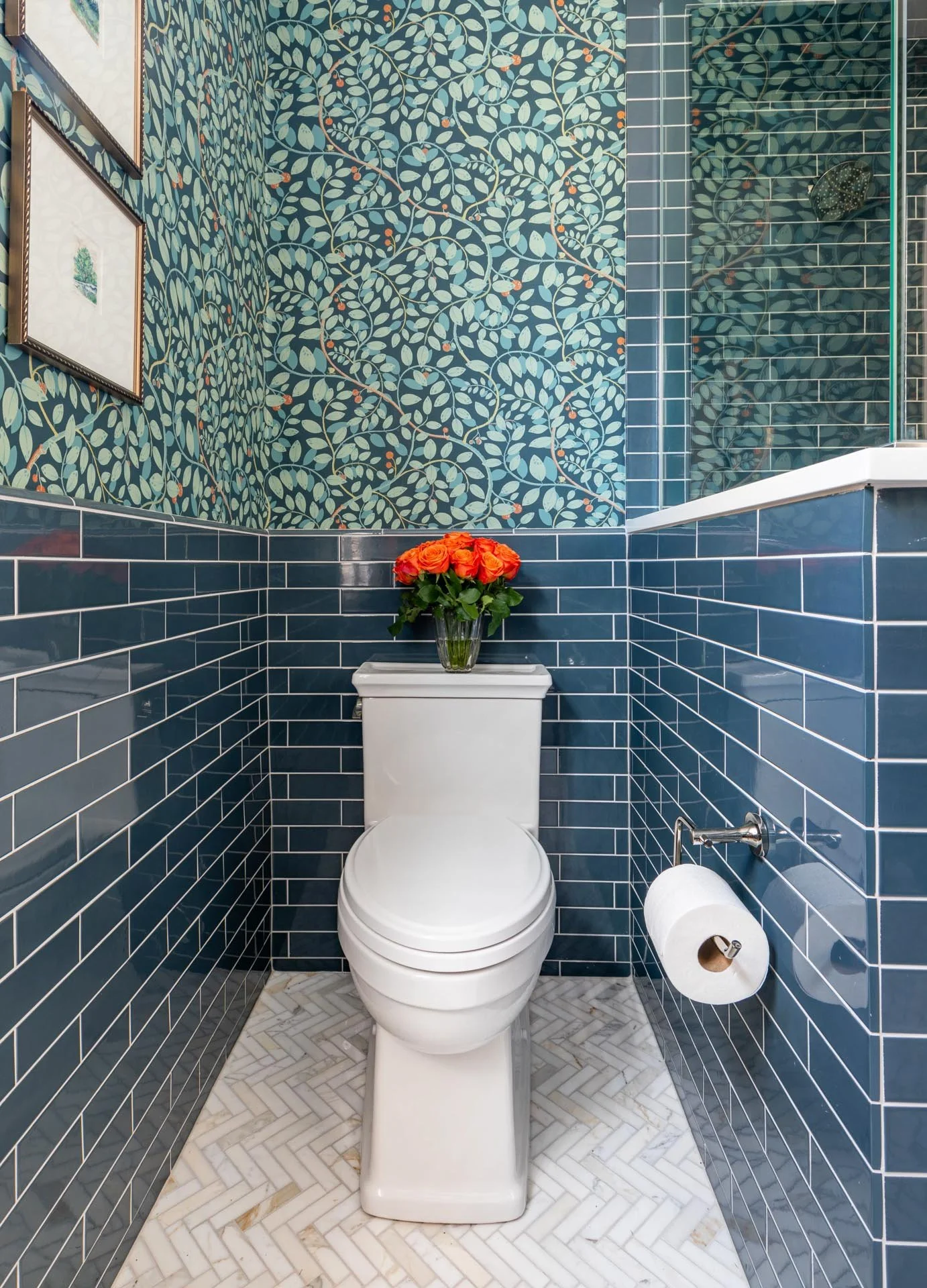 Lake Forest IL bathroom with bold botanical wallpaper, deep blue subway tile wainscoting, white toilet, and herringbone marble floor, designed by Wendy Nobriga Interiors.