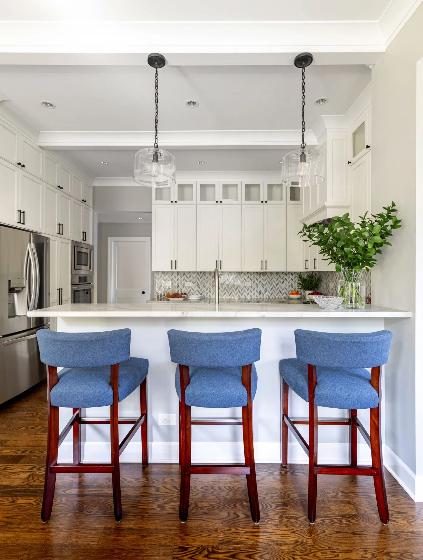 La Grange IL kitchen breakfast bar with quartzite counter, glass pendant lights, and three blue barstools by Wendy Nobriga Interiors.