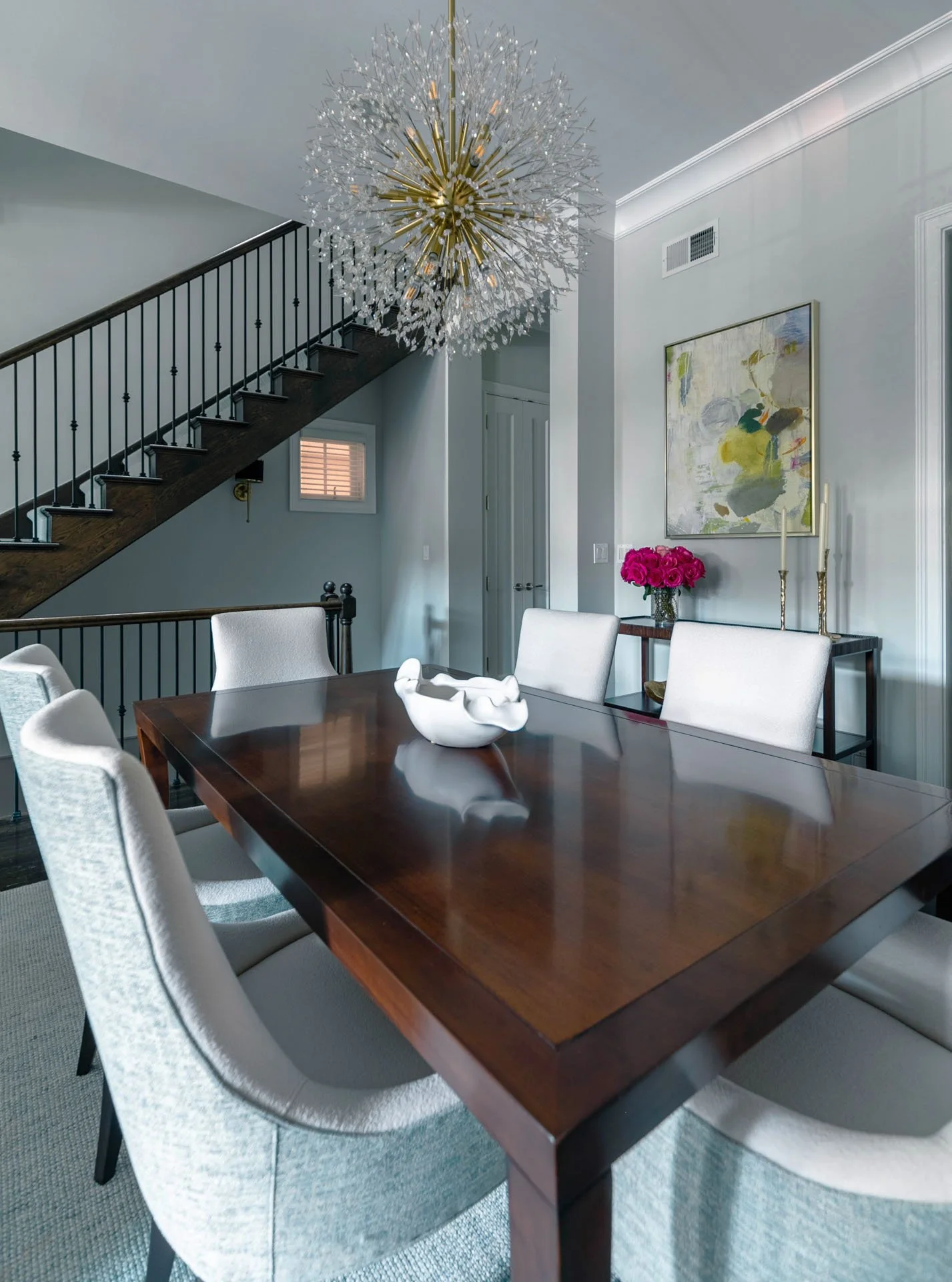 Lincoln Park Chicago dining room with modern chandelier, wood dining table, upholstered chairs, staircase view, and wall art designed by Wendy Nobriga Interiors