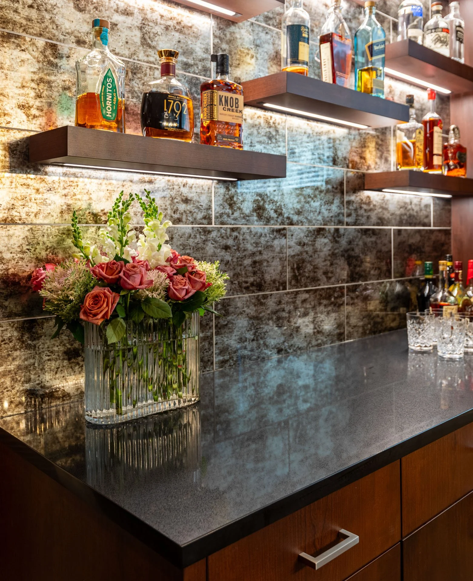 Close detail of liquor shelves and floral arrangement on dark stone bar counter in Roscoe Village Chicago basement, designed by Wendy Nobriga Interiors.