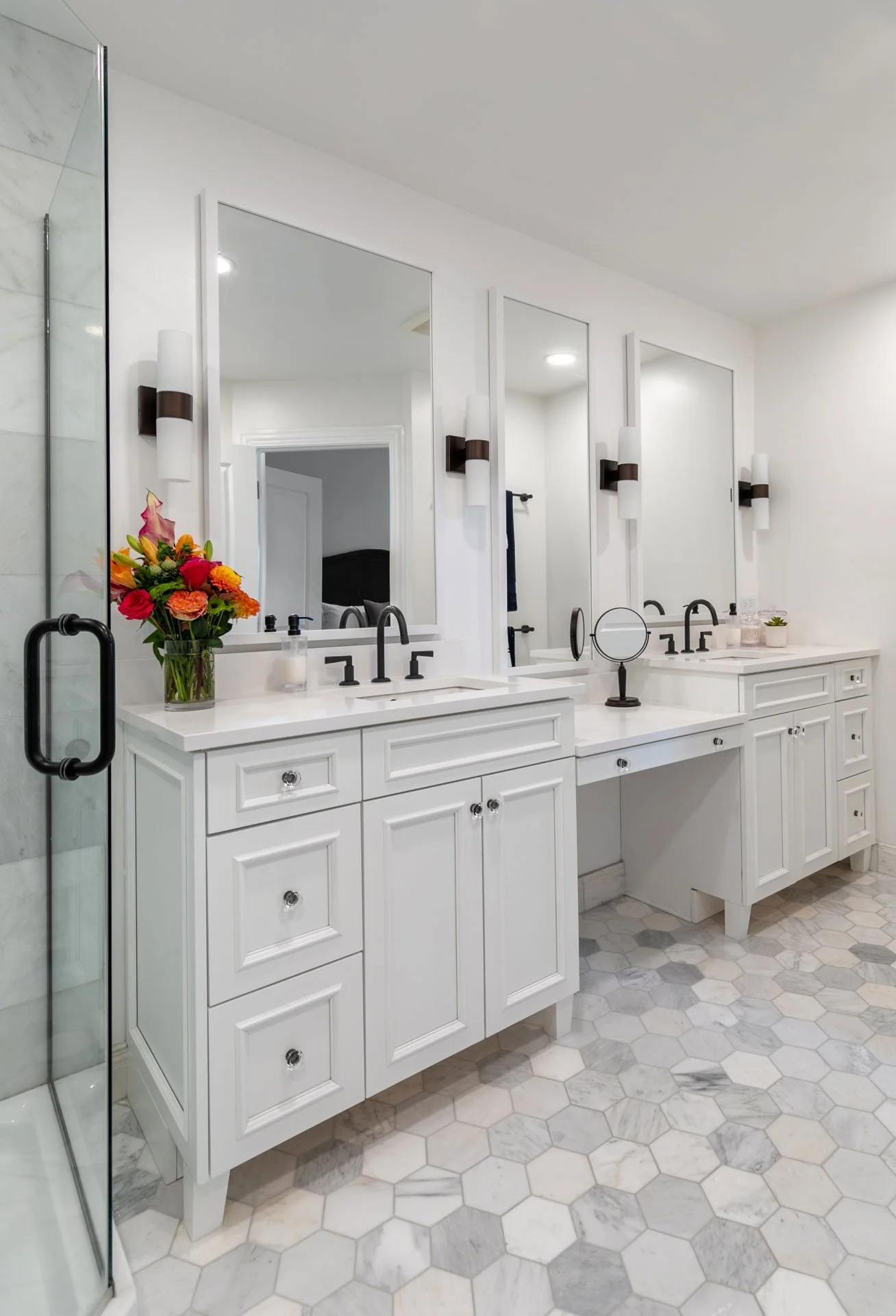 Primary bathroom in Des Plaines IL featuring a double vanity with bronze fixtures, white cabinetry, and marble hex tile flooring, designed by Wendy Nobriga Interiors.