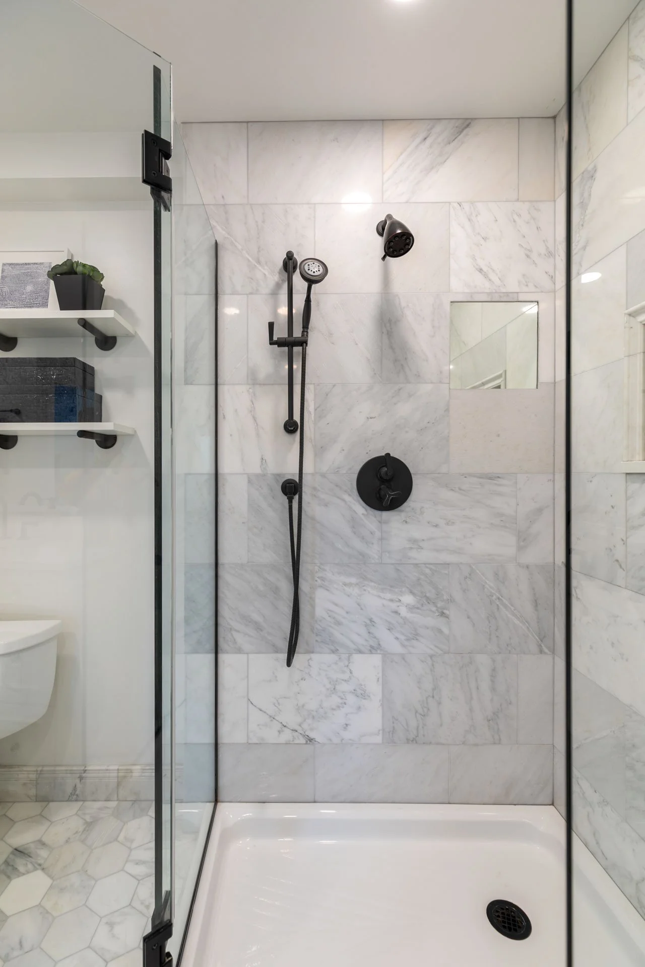 Primary bathroom in Des Plaines IL featuring a marble-tiled shower with bronze fixtures and a glass enclosure, designed by Wendy Nobriga Interiors.