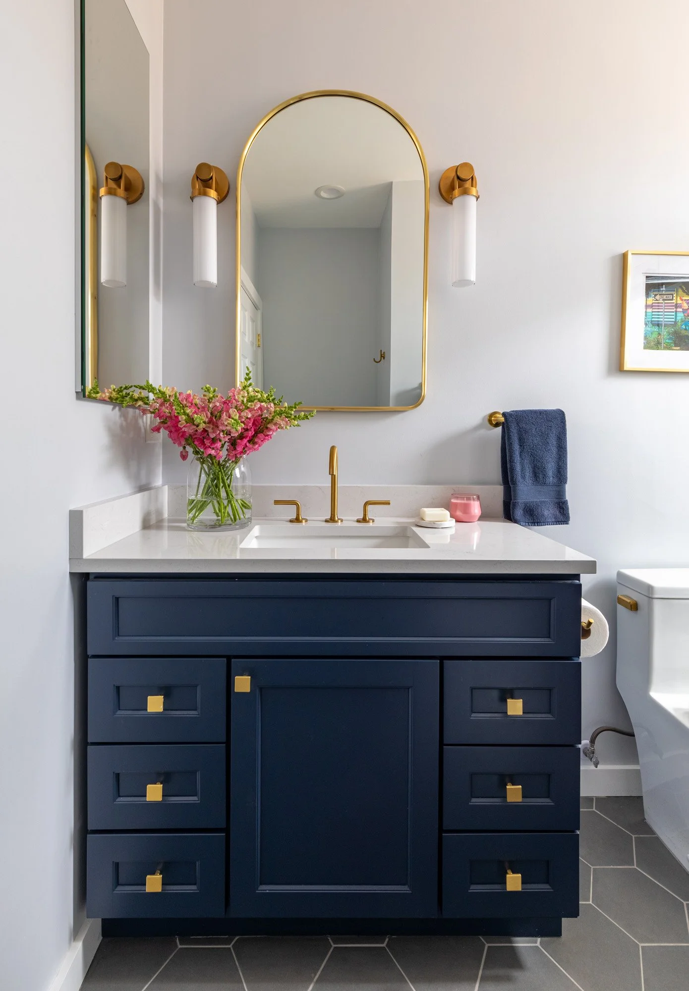 Custom navy blue bathroom vanity in a North Edgebrook Chicago home featuring a quartz countertop, brass plumbing fixtures, modern sconces, and contemporary design, designed by Wendy Nobriga Interiors.