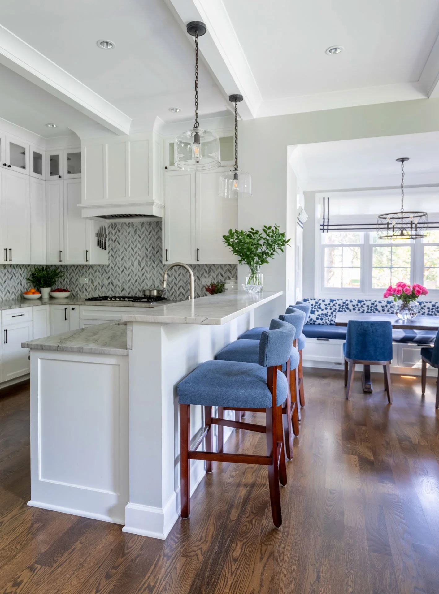 La Grange IL kitchen with quartzite bar counter, blue barstools, and view into breakfast nook with custom banquette by Wendy Nobriga Interiors.