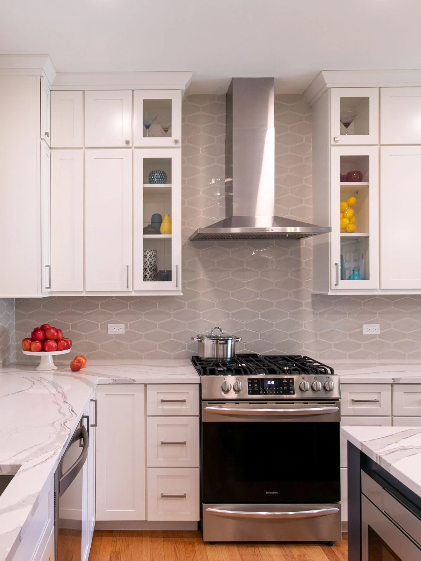 Oak Park, IL townhouse kitchen with stainless steel stove and hood, gray geometric backsplash, white cabinets, and quartz countertops, designed by Wendy Nobriga Interiors