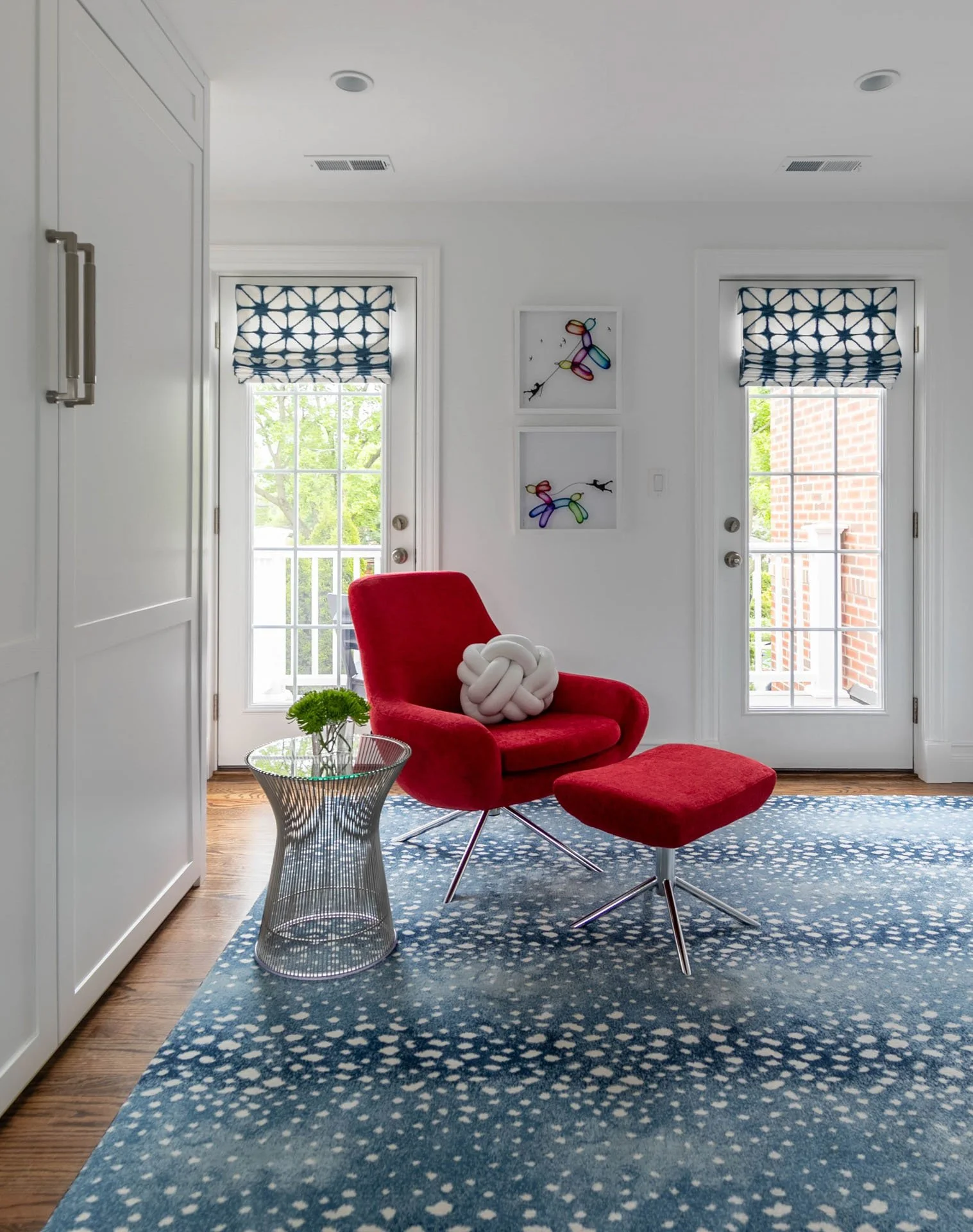 Guest bedroom and office in Edgebrook, Chicago, IL featuring a red chair and ottoman, playful balloon dog artwork, French doors, and blue patterned rug, designed by Wendy Nobriga Interiors.
