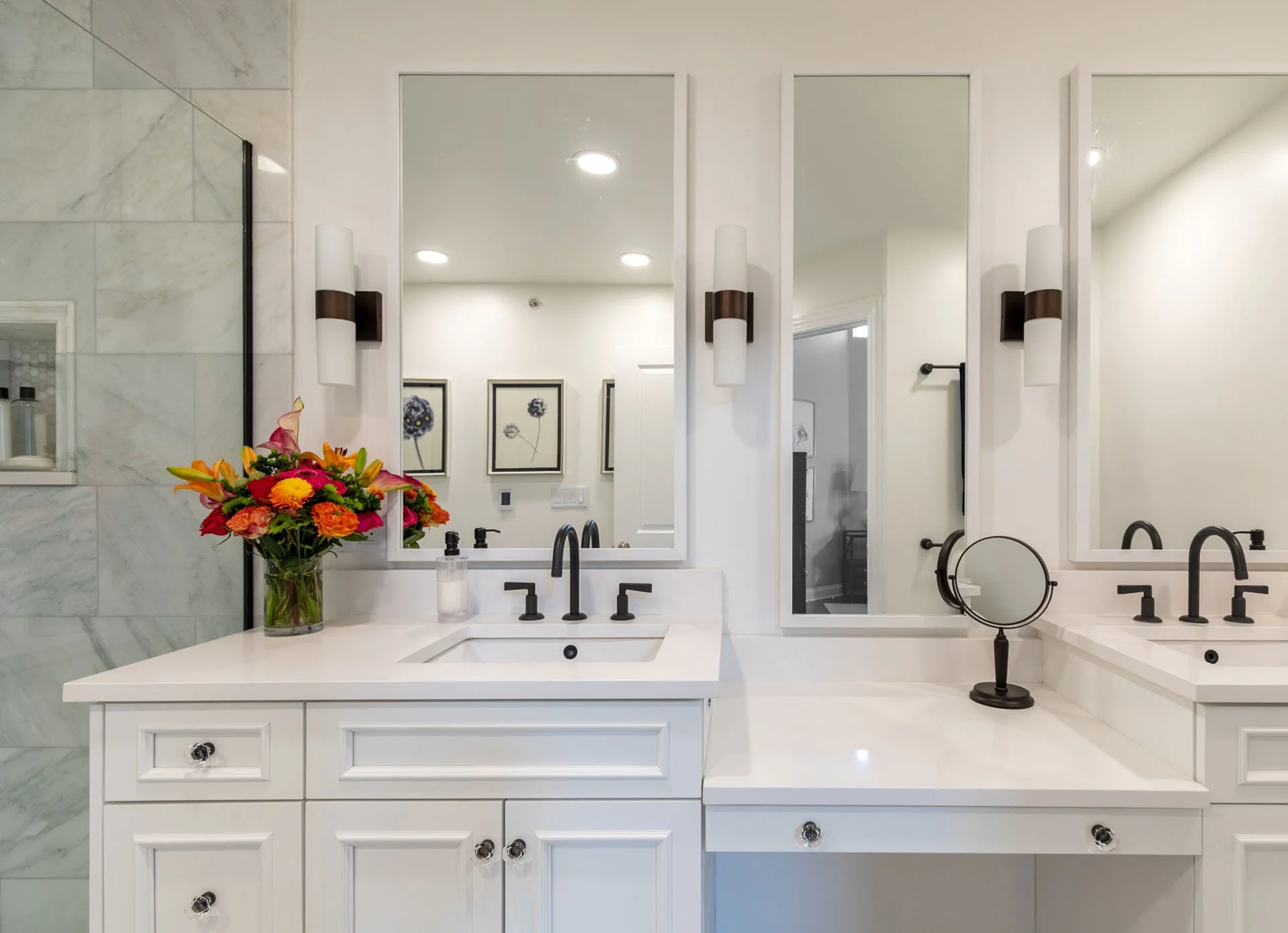 Primary bathroom in Des Plaines IL with a double vanity, white cabinetry, bronze fixtures, and a bright floral arrangement, designed by Wendy Nobriga Interiors.