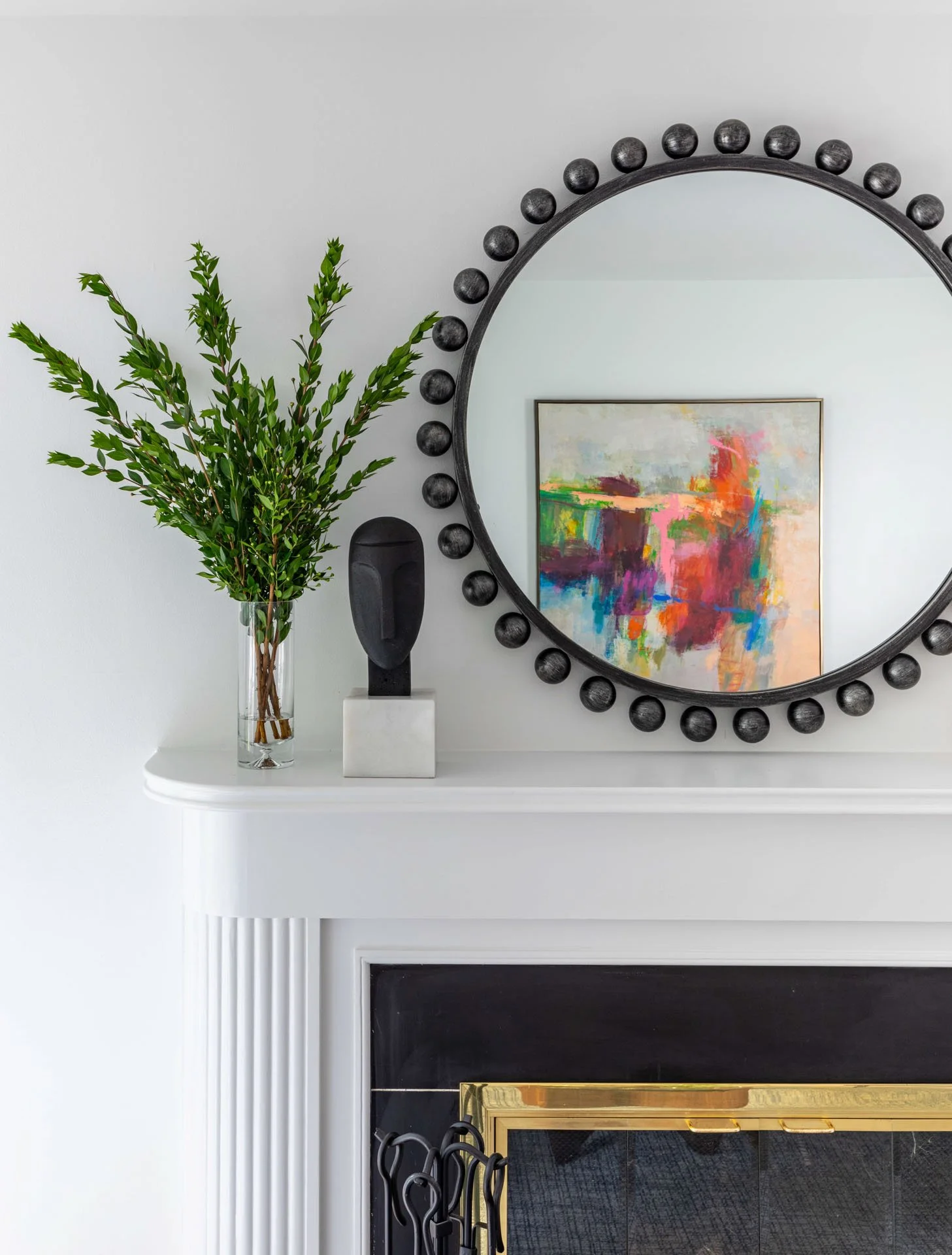 Wildwood Chicago, IL living room fireplace detail with black round mirror, greenery in vase, and reflection of colorful abstract artwork.