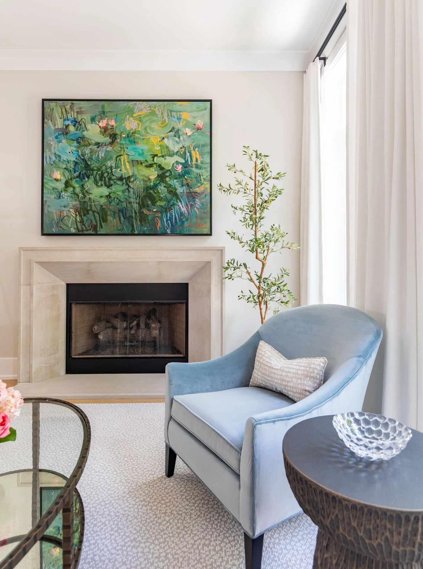 Detail view of blue armchair, stone fireplace, and abstract artwork in Roscoe Village Chicago living room, designed by Wendy Nobriga Interiors.