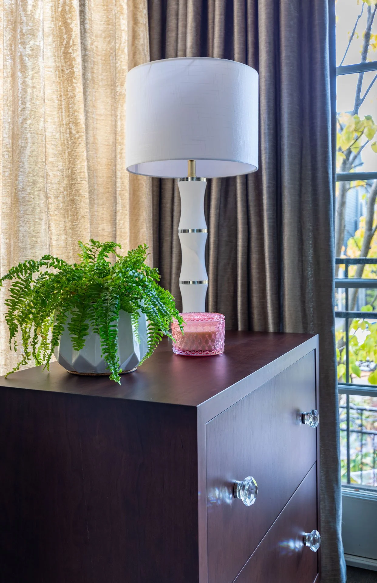 Roscoe Village Chicago home office side chest with crystal knobs, white table lamp, green fern in a geometric planter, and pink glass candle, designed by Wendy Nobriga Interiors.