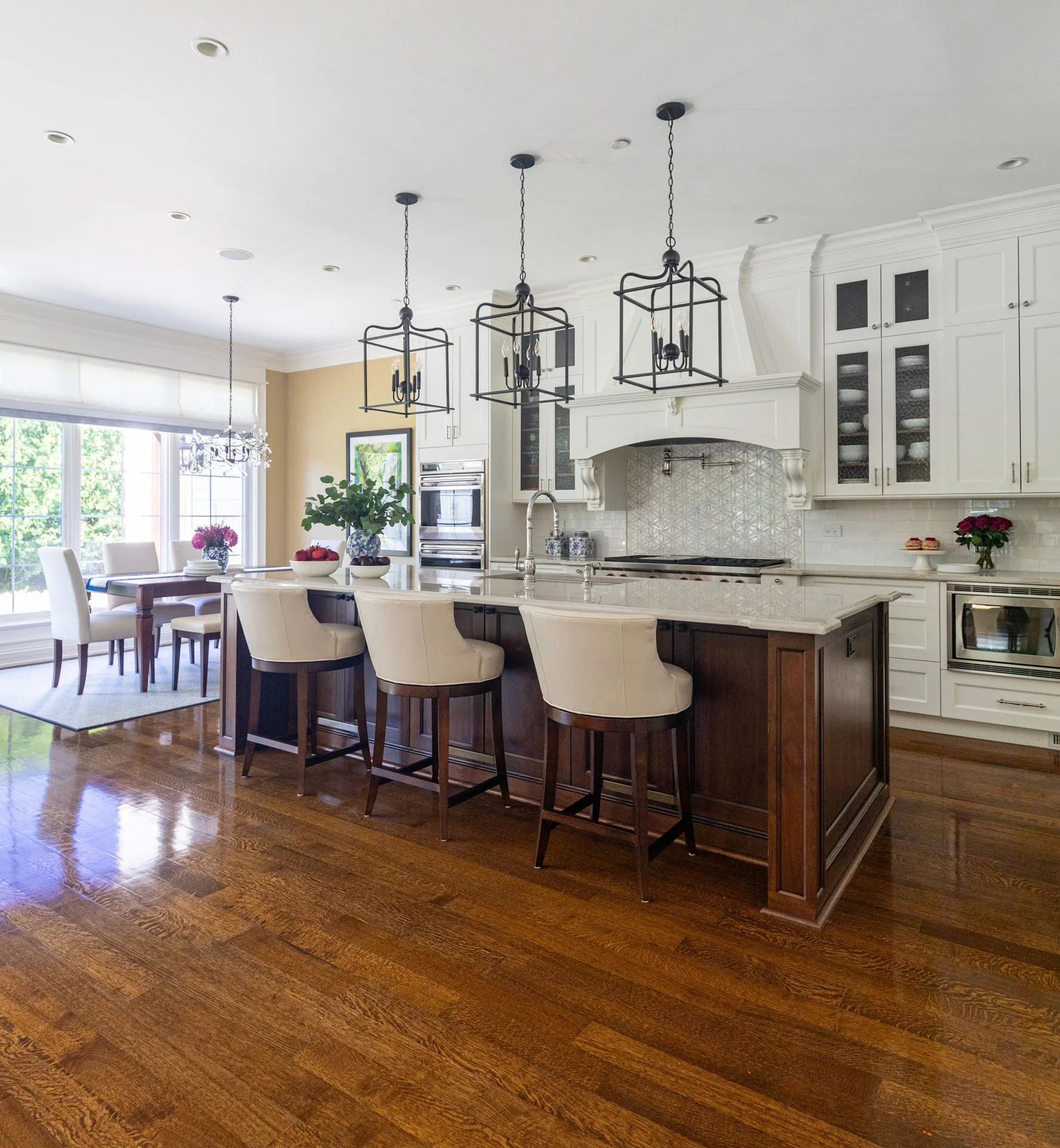 Lincolnwood IL kitchen featuring a dark wood island with quartzite countertops, white cabinetry, black lantern pendants, and a view into the adjacent dining area, designed by Wendy Nobriga Interiors.