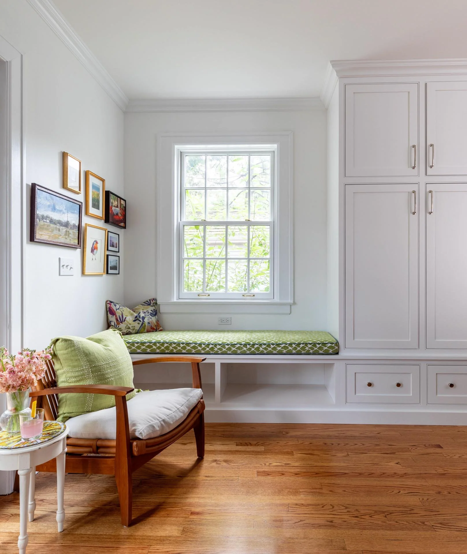 Lake Forest IL kitchen corner with built-in window bench featuring a green cushion, white cabinetry with storage drawers, and wood flooring, designed by Wendy Nobriga Interiors.