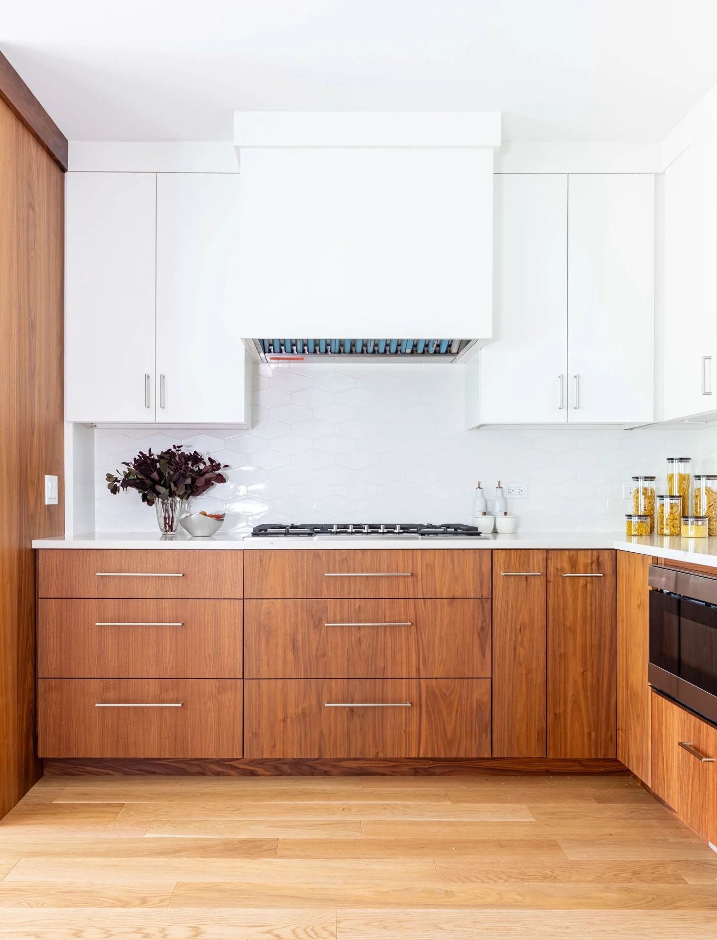 Wildwood Chicago IL kitchen range wall with white upper cabinets, walnut wood base cabinets, hexagon tile backsplash, and modern vent hood, designed by Wendy Nobriga Interiors.