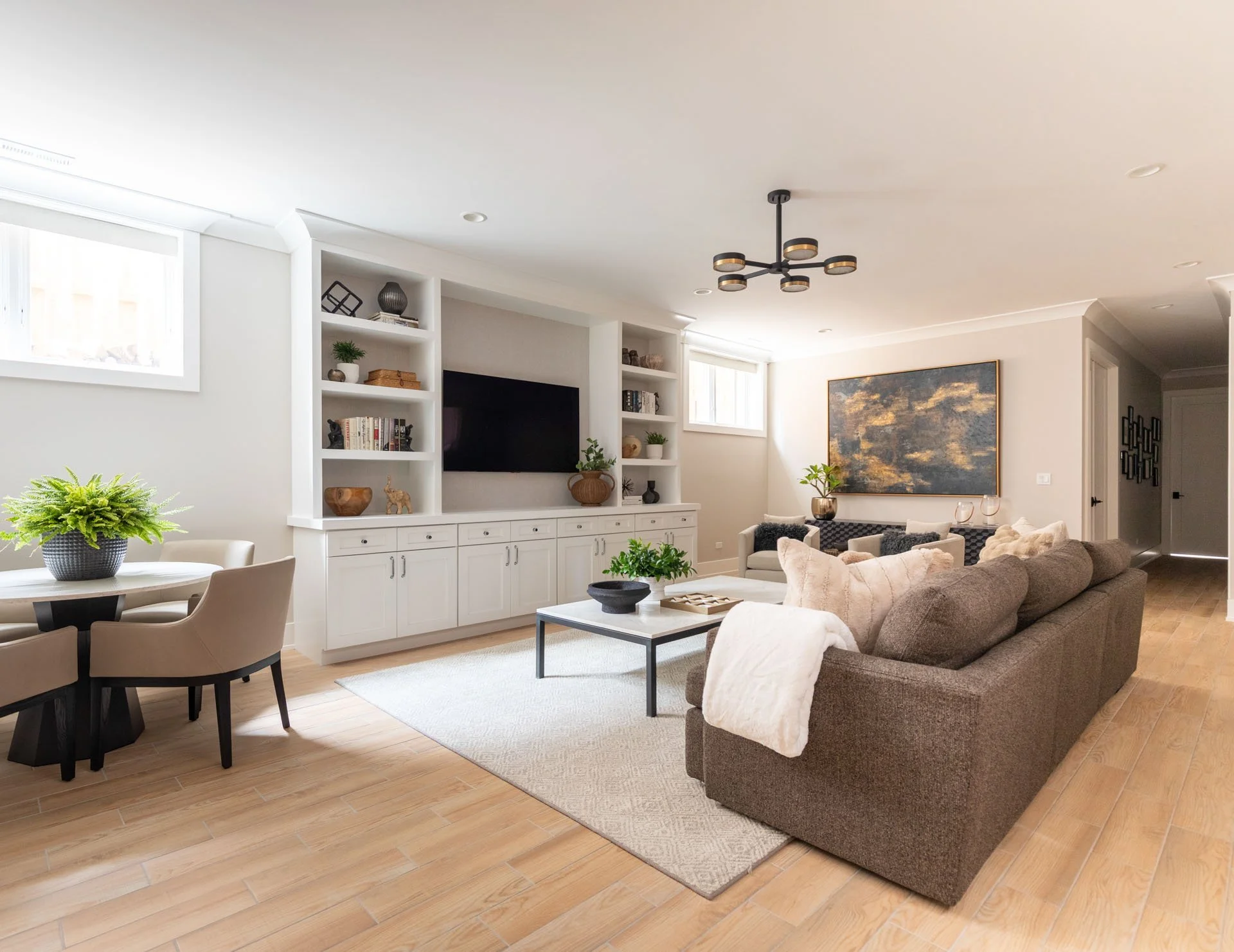 Angled view of Roscoe Village Chicago basement family room with sectional sofa, media wall, lounge chairs, game table, and large artwork, designed by Wendy Nobriga Interiors.