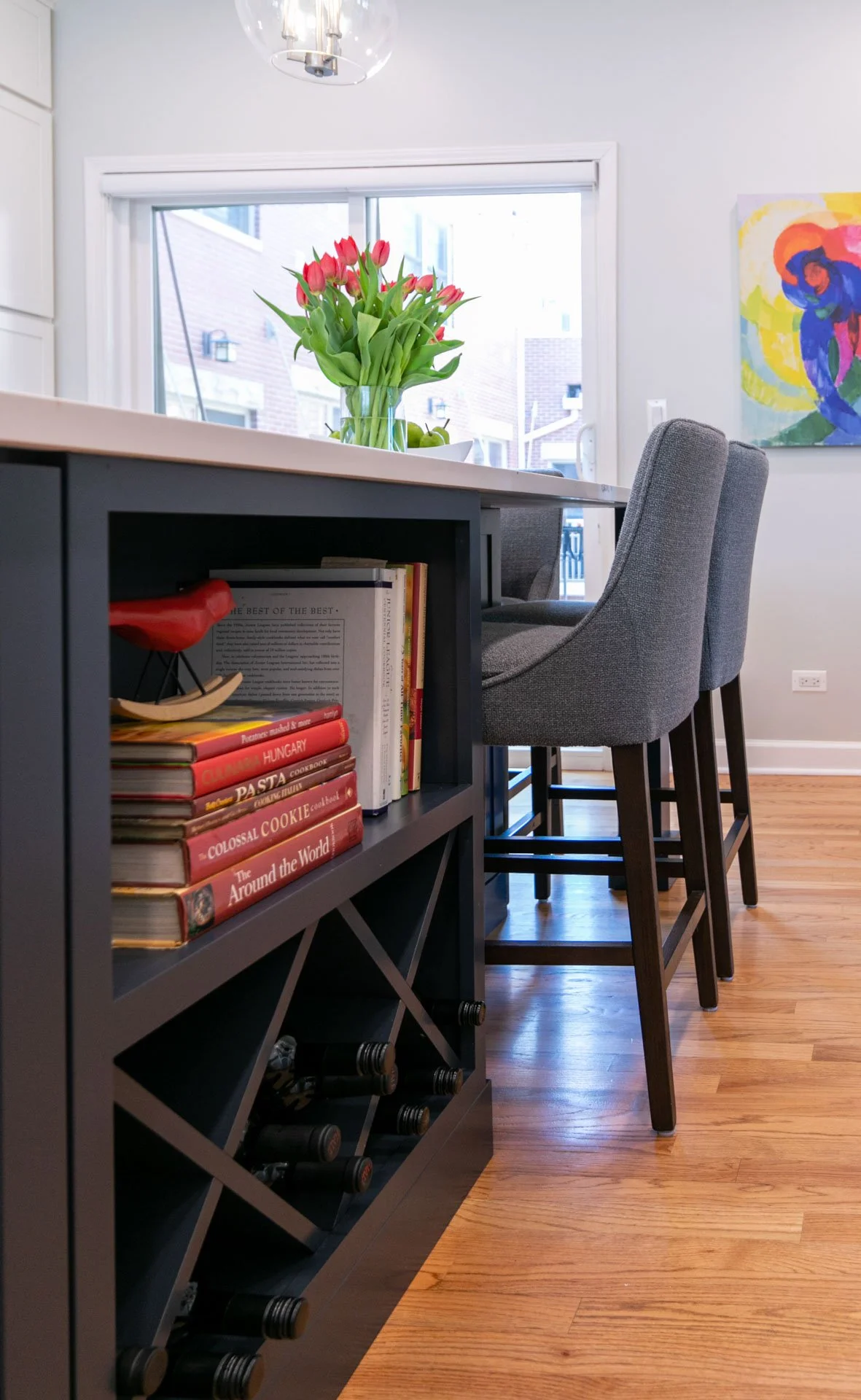 Kitchen island in Oak Park, IL townhouse with built-in bookshelf, wine storage, and quartz countertop with gray upholstered bar stools, designed by Wendy Nobriga Interiors