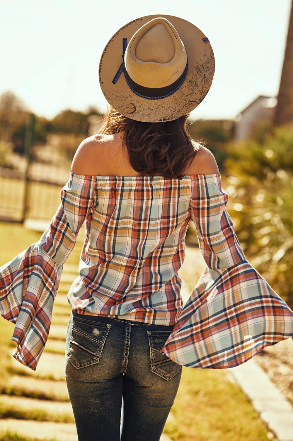 Backshot fashion photography of a model wearing a plaid off shoulders top and a cowboy hat